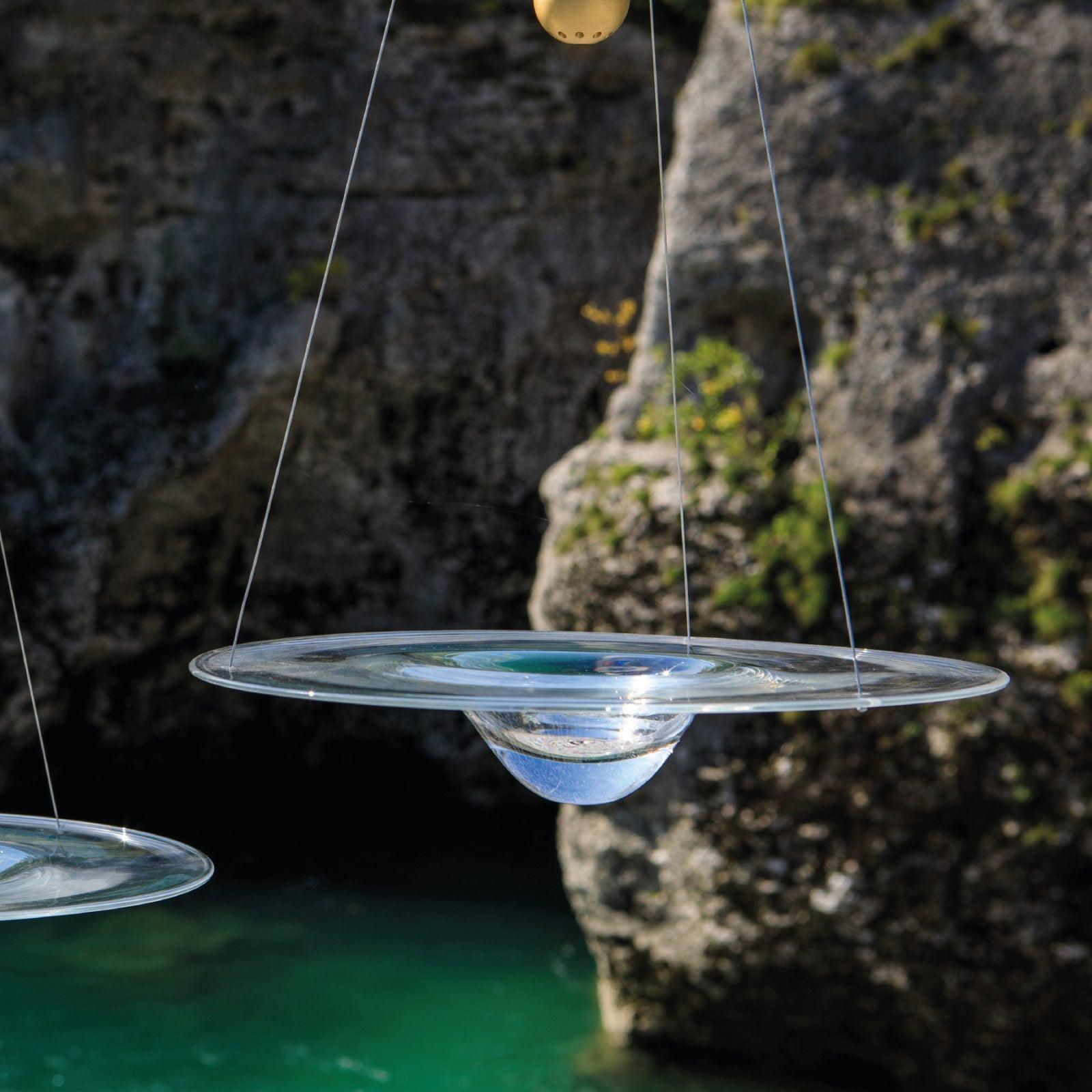 Glass disc pendants pictured beside rocks and water