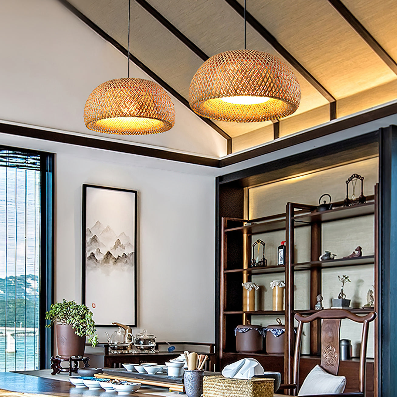 Two lit bamboo dome pendants on black cords above a tea table, teaware, chair, shelves and landscape artwork