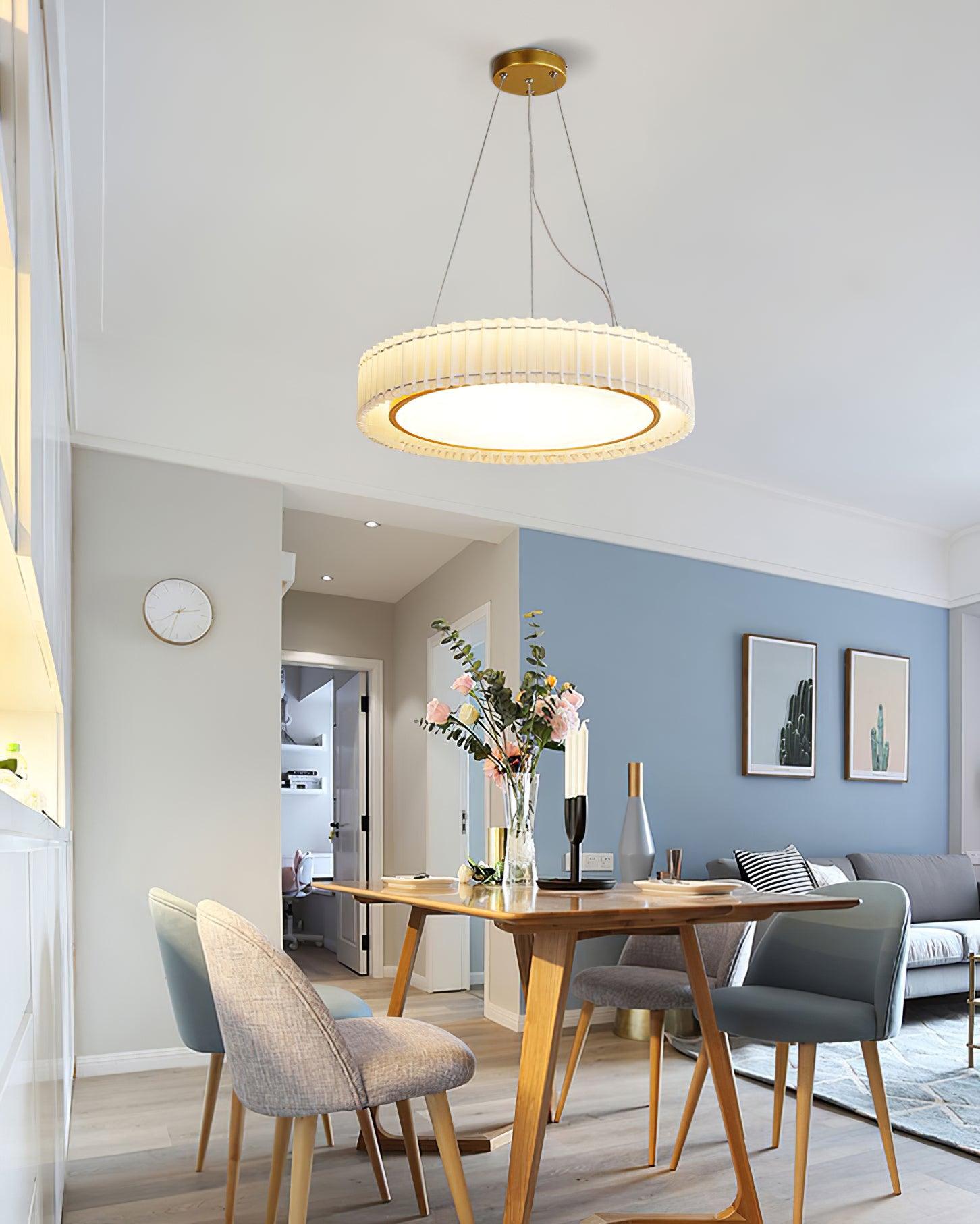 Lit pleated pendant above a wooden dining table with flowers and mixed chairs in an open living and dining room