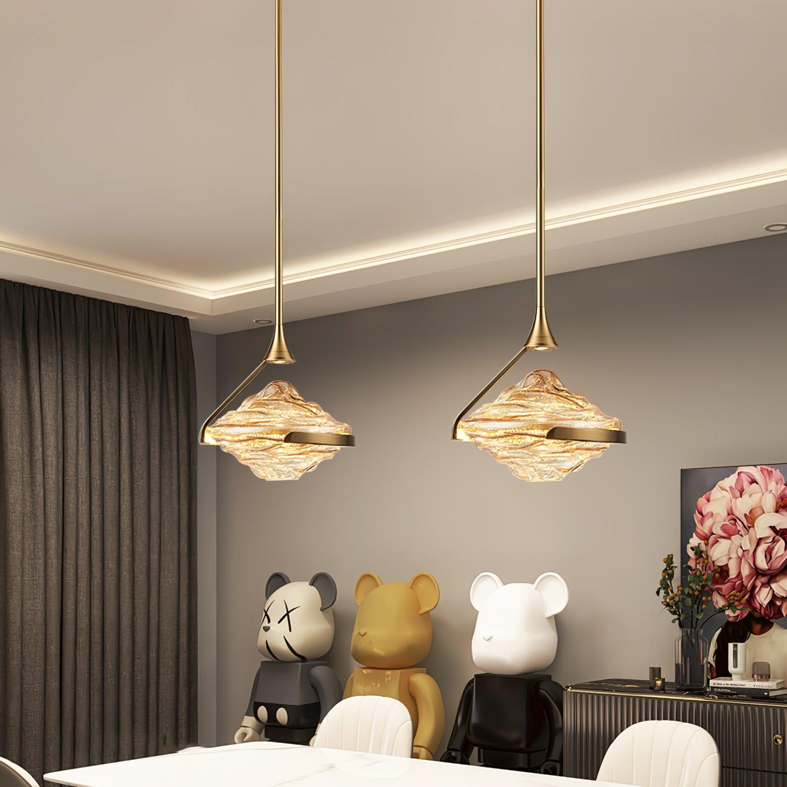 Closer dining-room view of two illuminated amber-looking glass pendants, white chairs and flower artwork