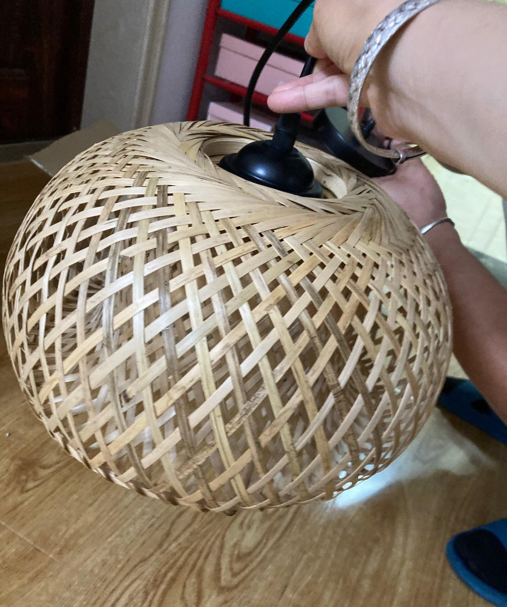 Hand holding upper black cable and fitting of natural woven dome shade above wooden floor