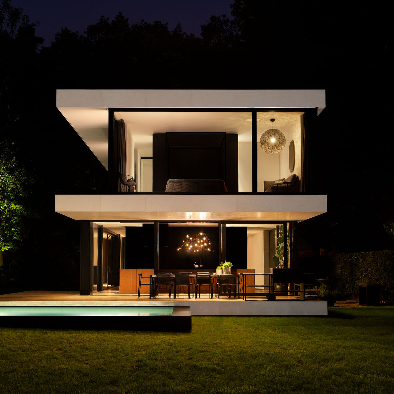 Lit looping-wire pendant visible through downstairs dining-room windows of a house at night