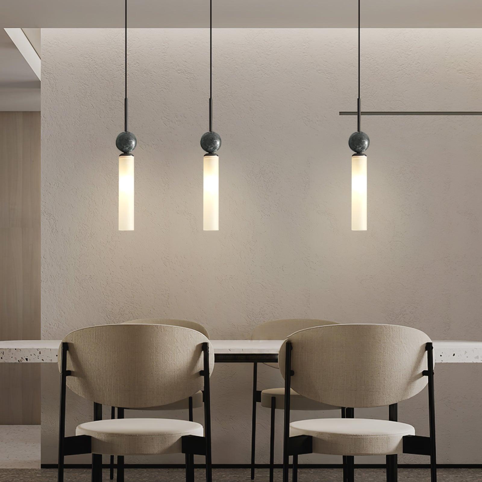 Wide dining view of three black-stem marble-sphere pendants with white tubes over counter and two pale chairs