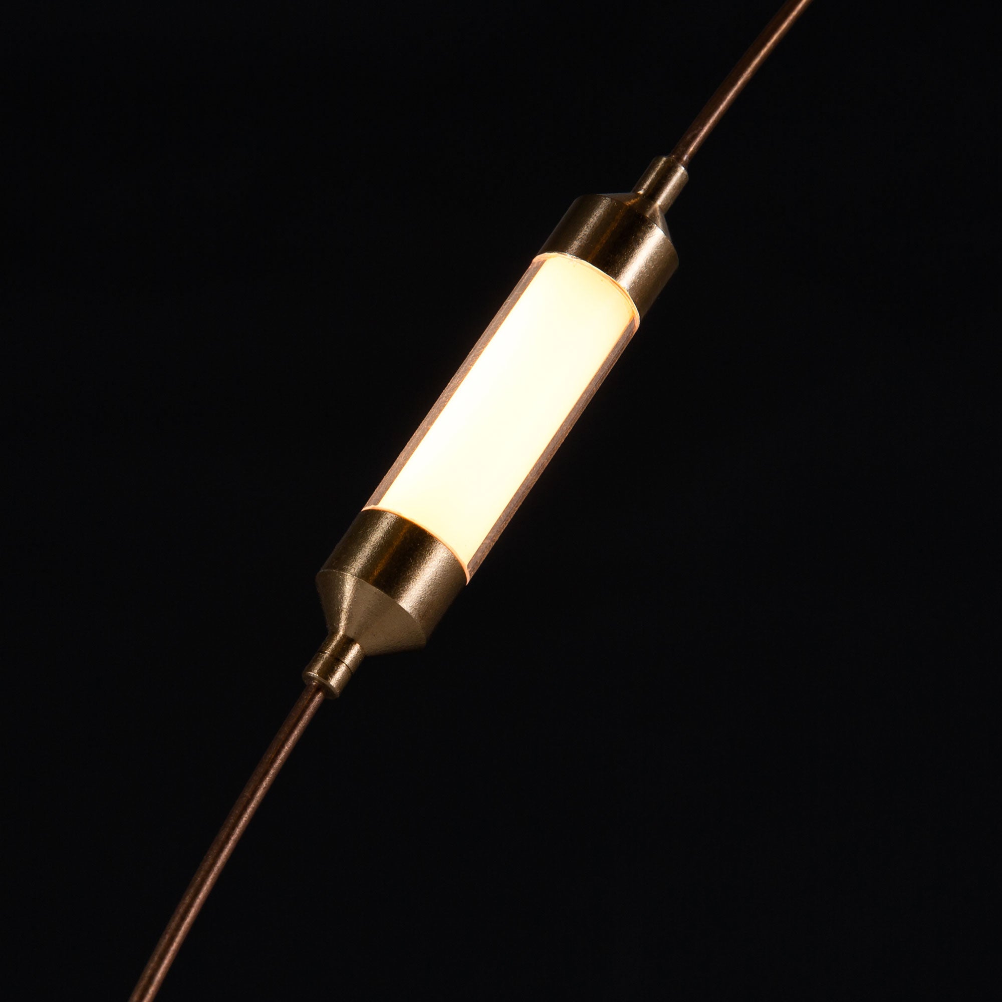Close white glowing cylindrical diffuser between gold-tone tapered end caps and thin wires