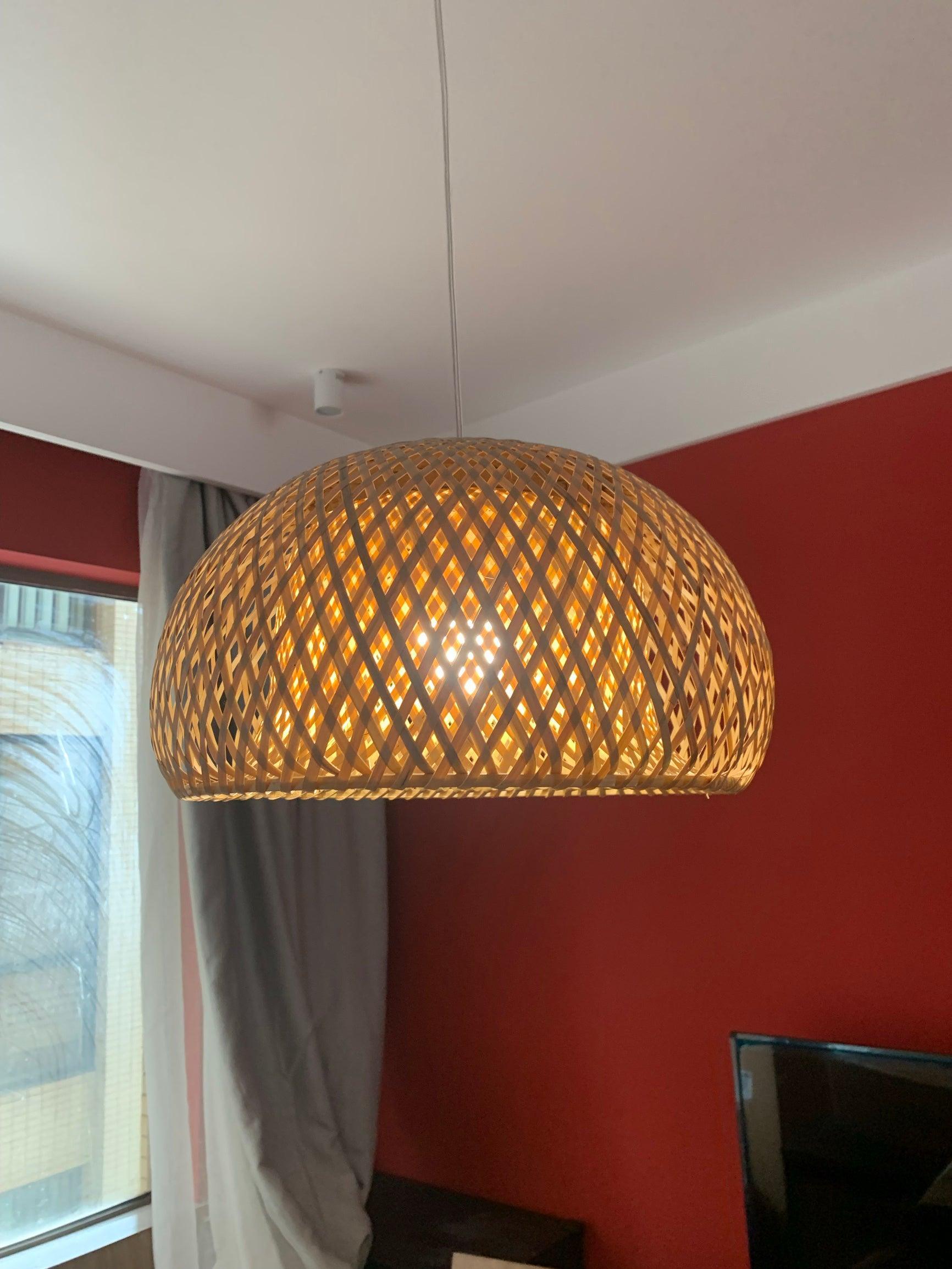 Close view of lit bamboo dome with diamond weave and curved profile before a red wall and curtained window