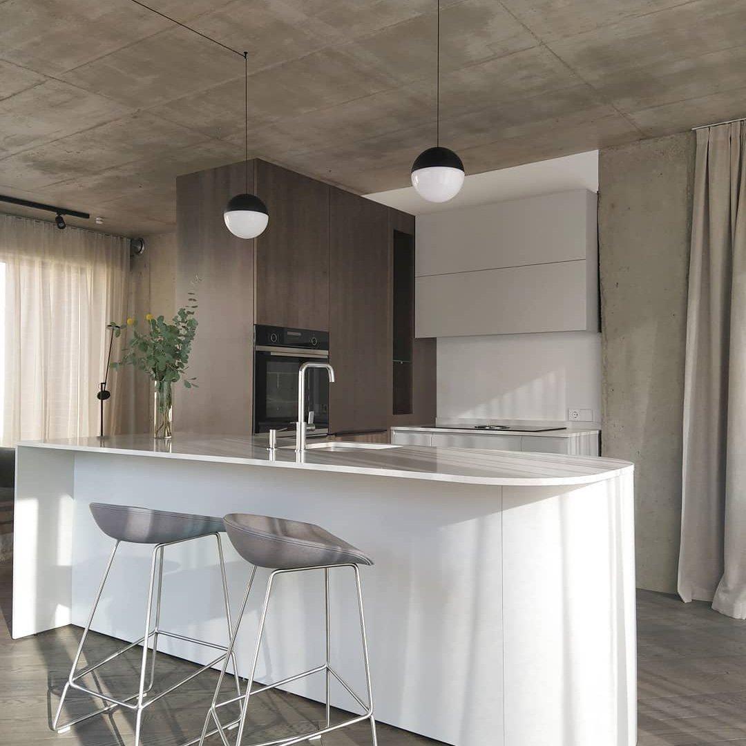 Two black-top pale-lower globe pendants above a white kitchen island with stools, sink and wood cabinets