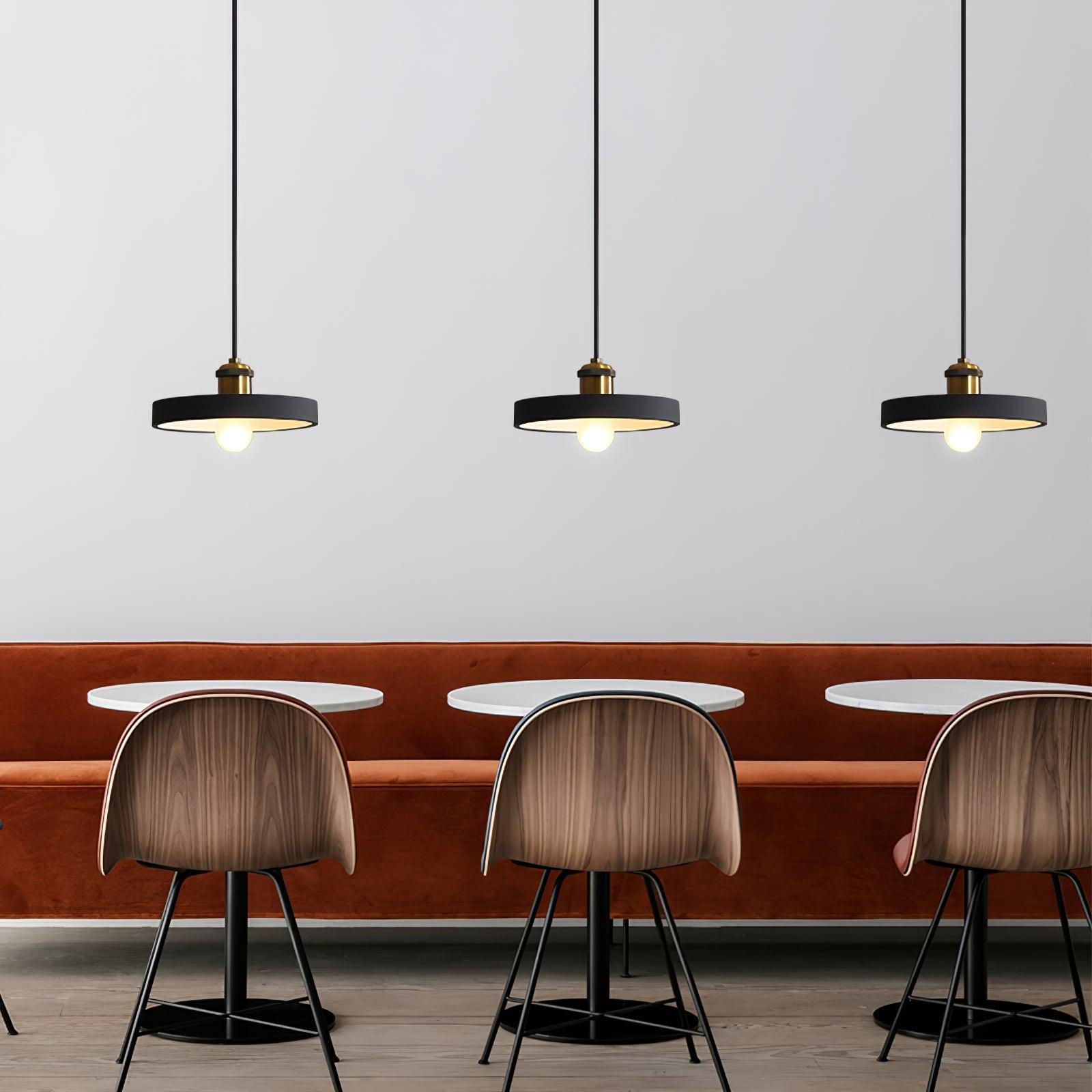 Three dark shallow disc pendants above bar seating