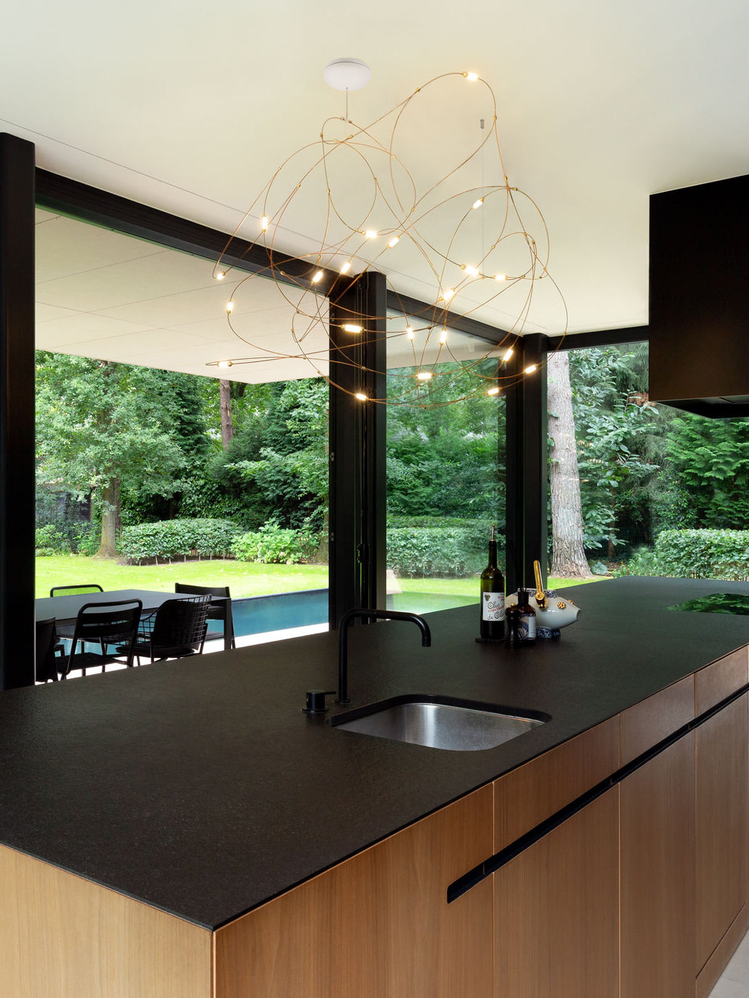 Airy gold-tone wire-loop pendant above a kitchen island and sink with garden views