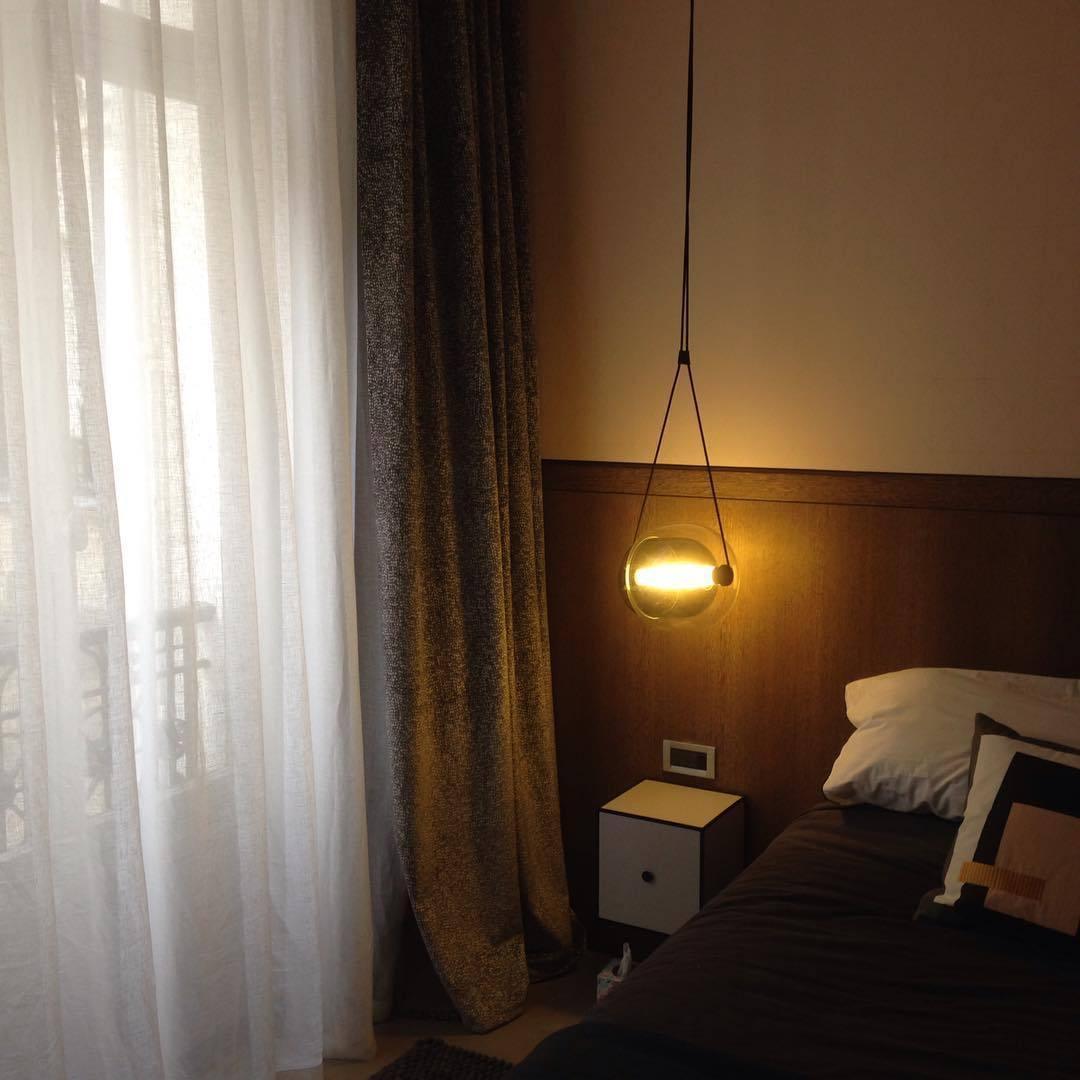 Small illuminated capsule pendant beside a bed