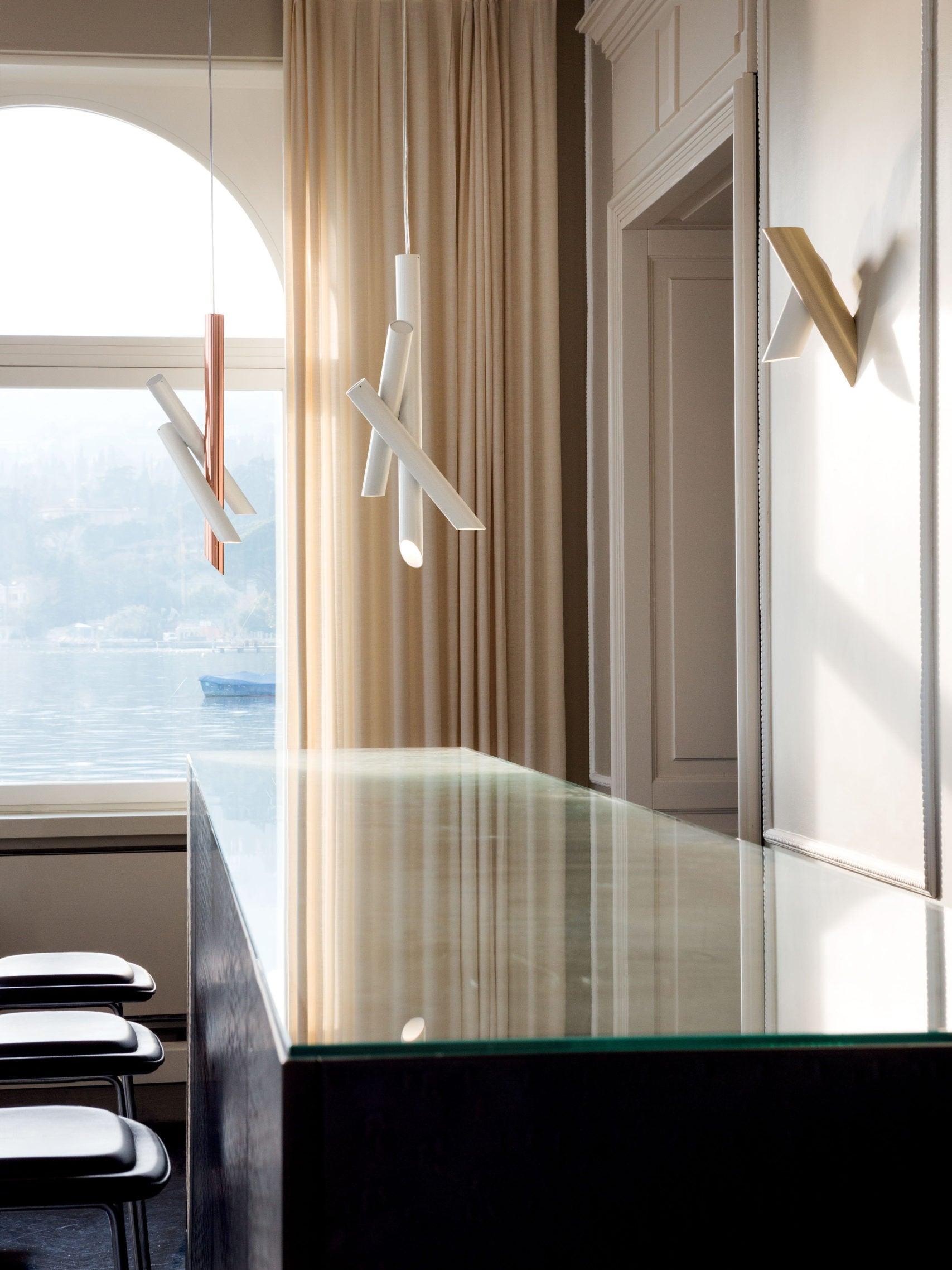 White and rose-gold Tubes pendants reflected near a tall window and beige curtains