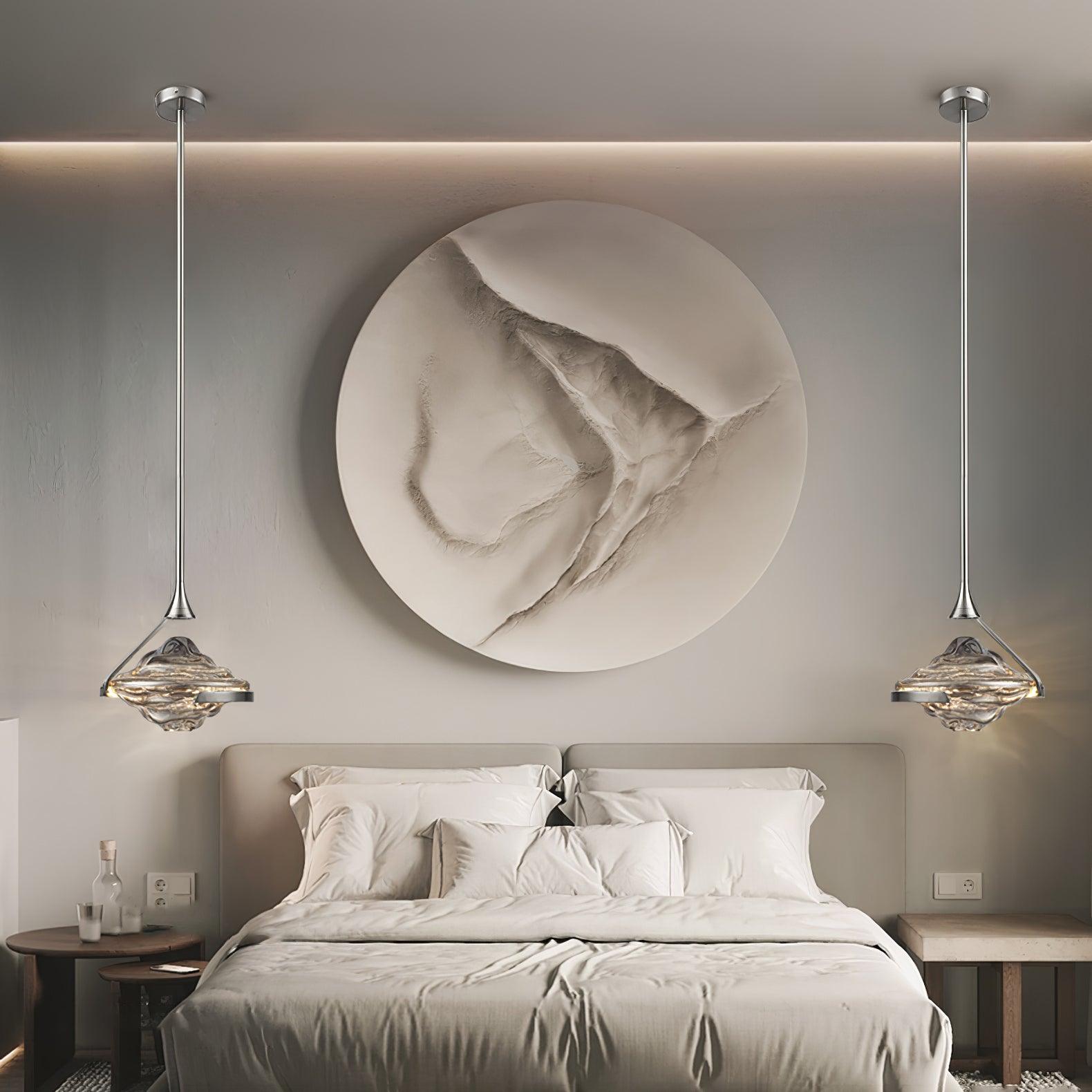 Two chrome-looking glass pendants flanking a pale bed beneath large circular wall artwork, each with a round canopy