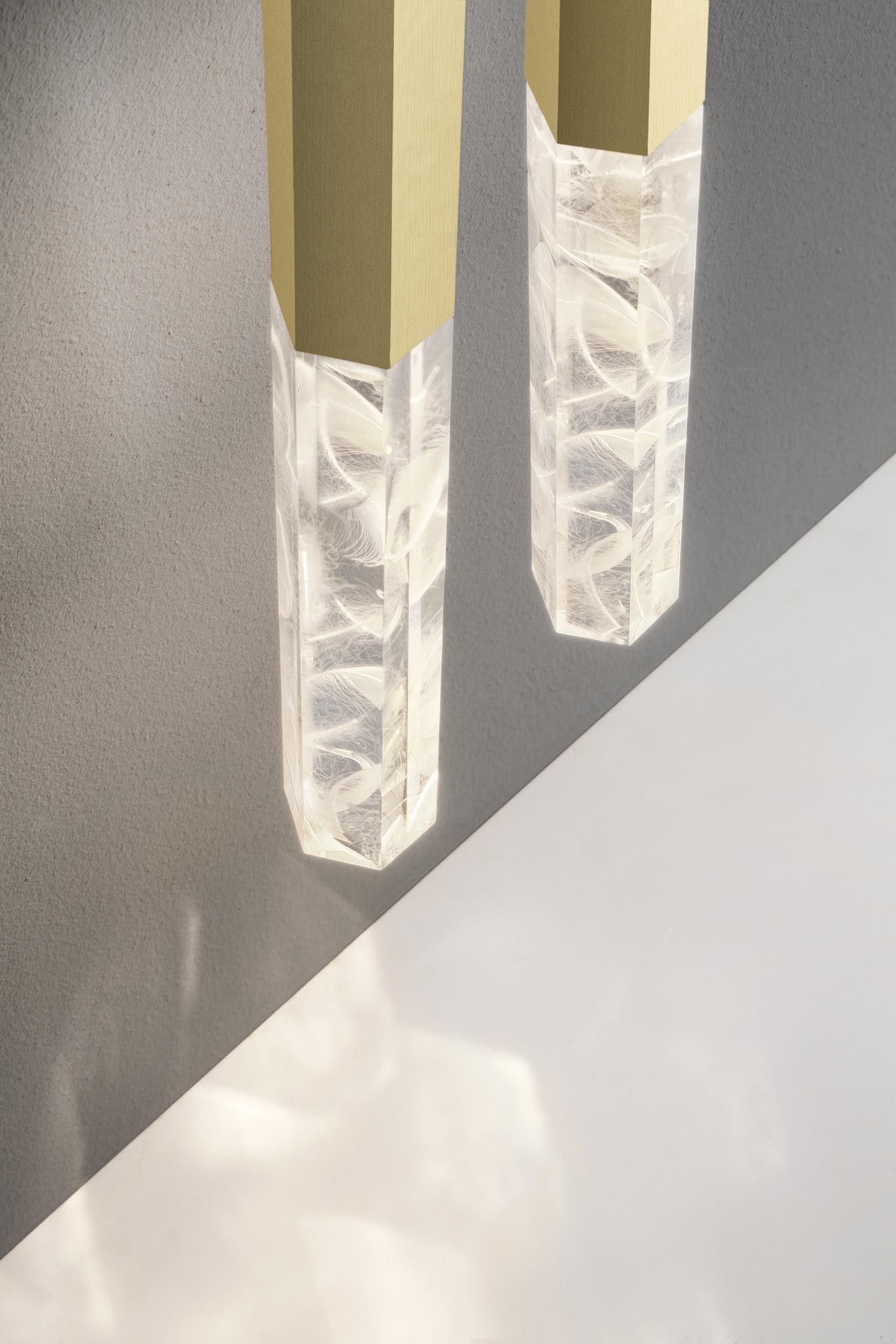 Close two angular gold-tone shafts and illuminated clear feather-patterned ends above a pale surface