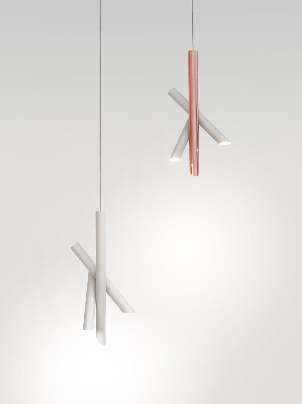 White and rose-gold Tubes pendants suspended at different heights against a grey wall