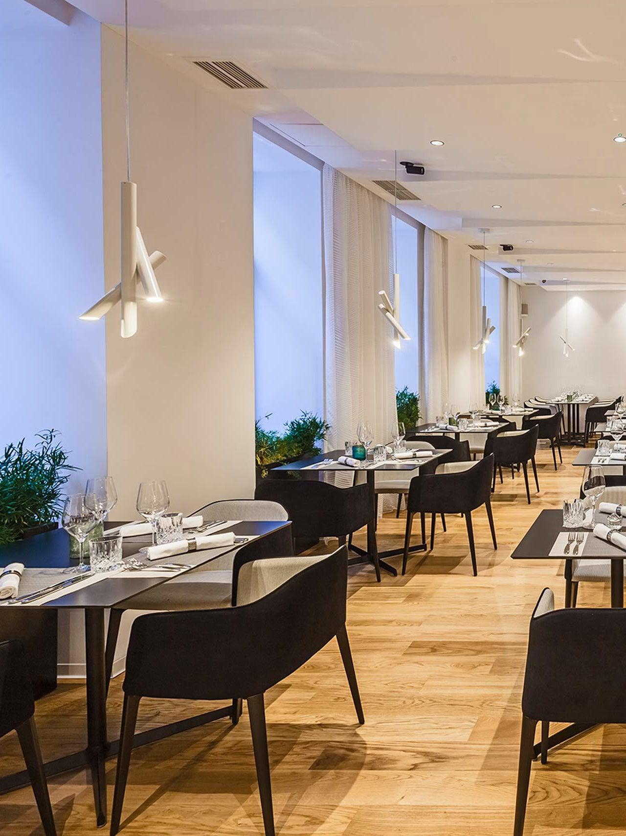 White Tubes pendants beside windows above restaurant tables set for dining