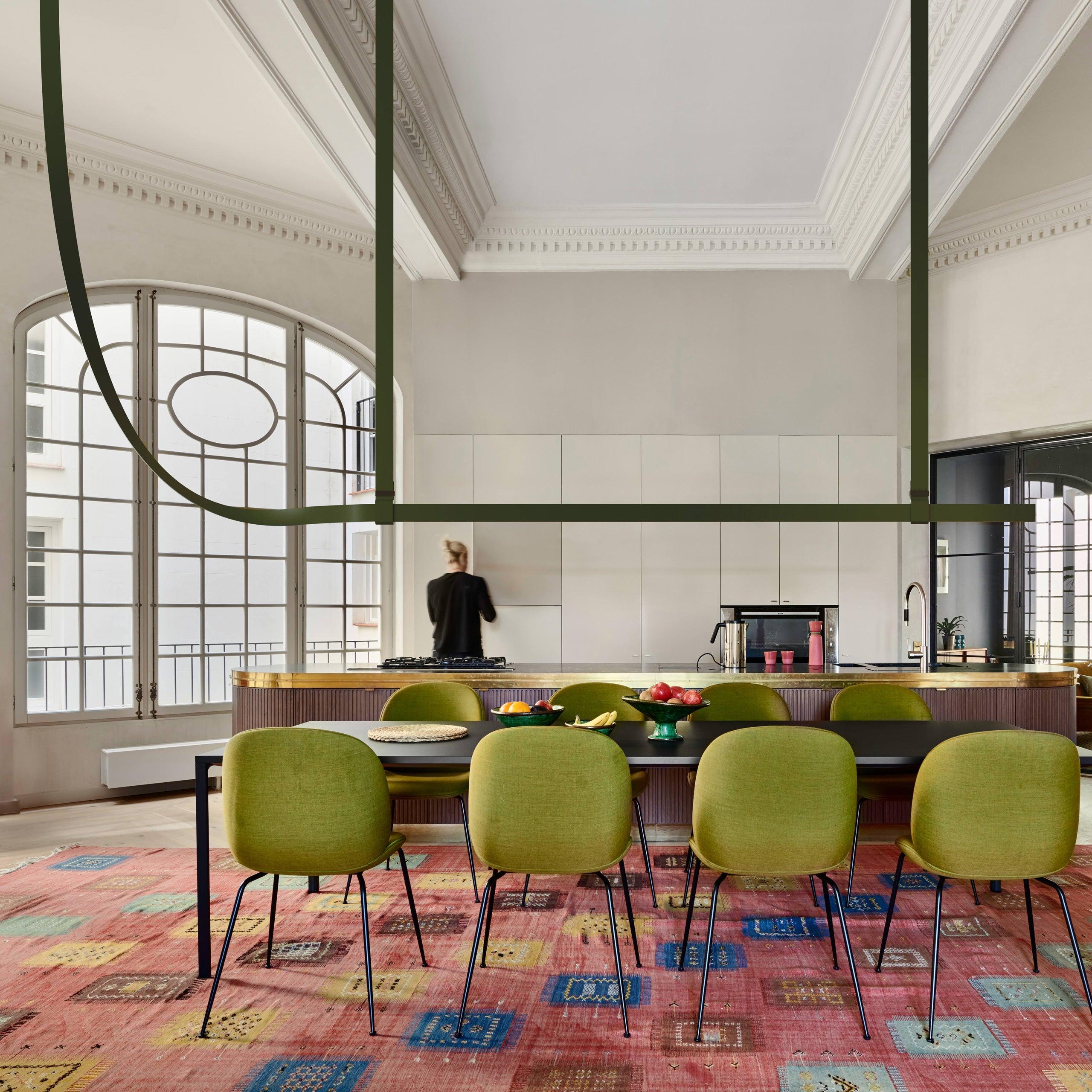 Dark green linear pendant above a dining table with green chairs and a colourful rug