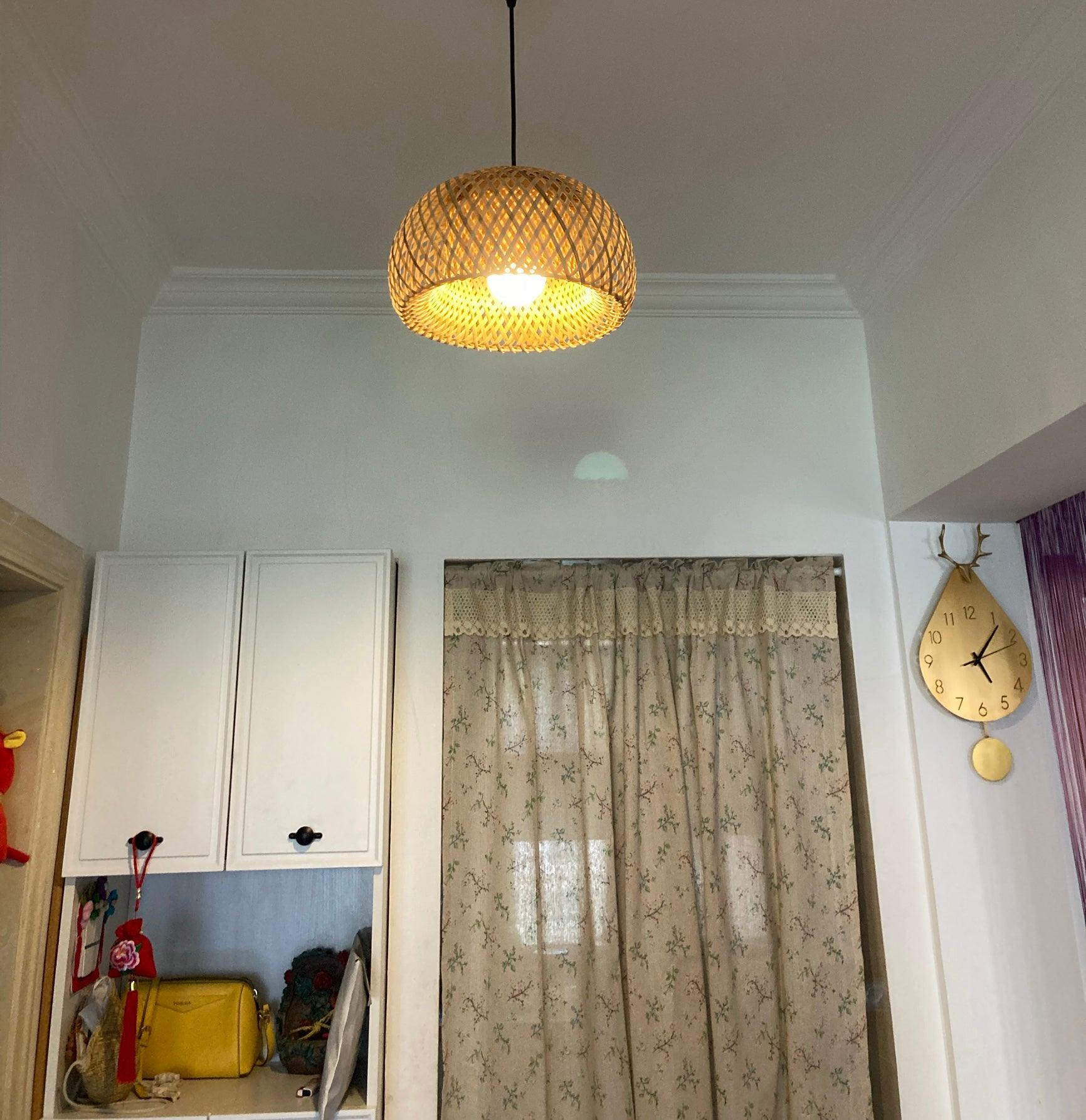 Lit bamboo dome on black cord above white cupboards, patterned curtains and a wooden drop-shaped wall clock