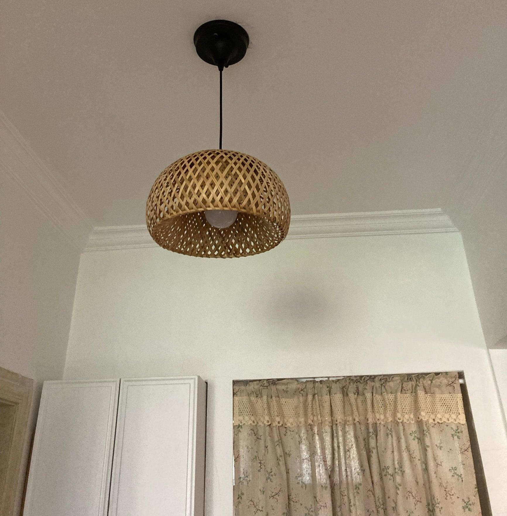 Unlit bamboo dome and white globe bulb on black suspension, with white cupboards and floral curtain below