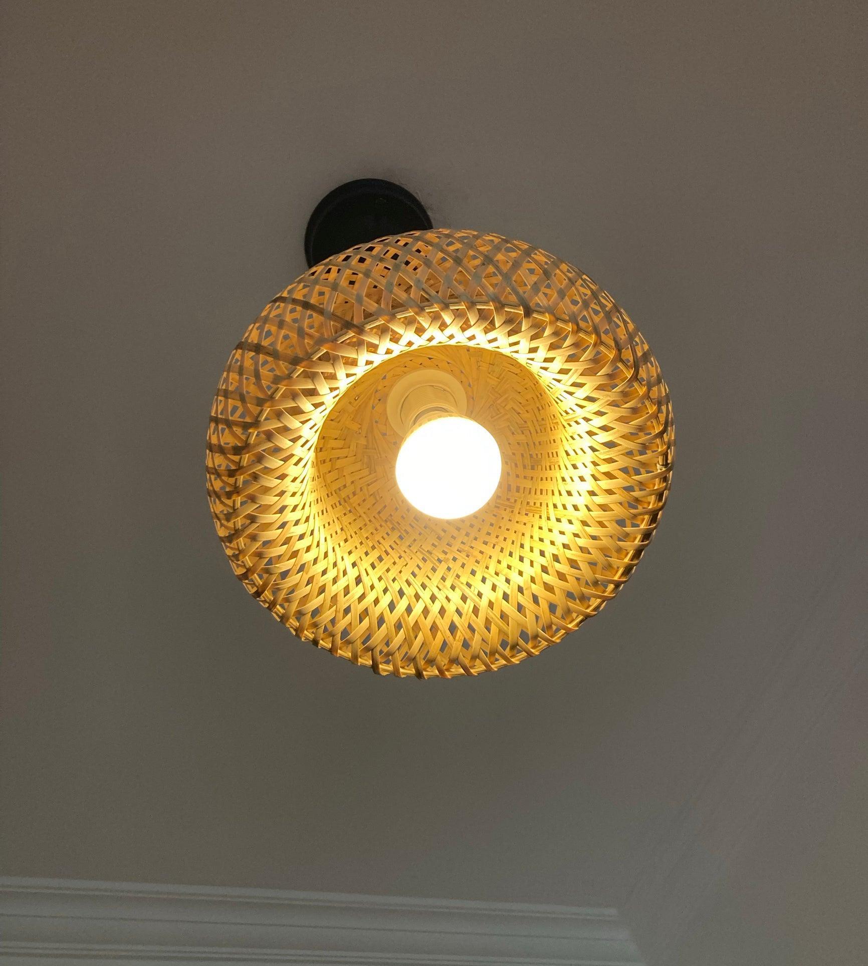 Underside close-up of glowing round bulb and socket inside bamboo dome, with layered weave and wrapped lower rim