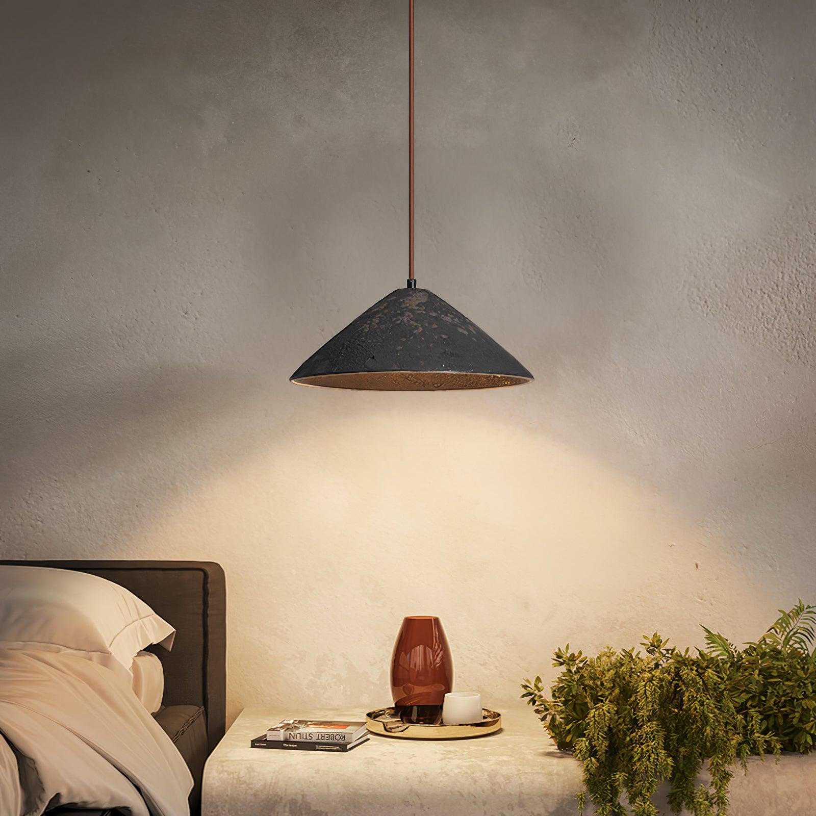 Black mottled cone pendant beside a bed, above a stone bench with books, a red vase, cup and trailing greenery