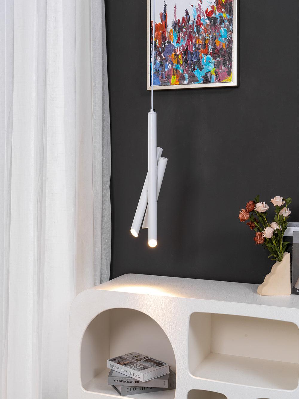 Illuminated white Tubes pendant casting light above a pale cabinet on a dark wall