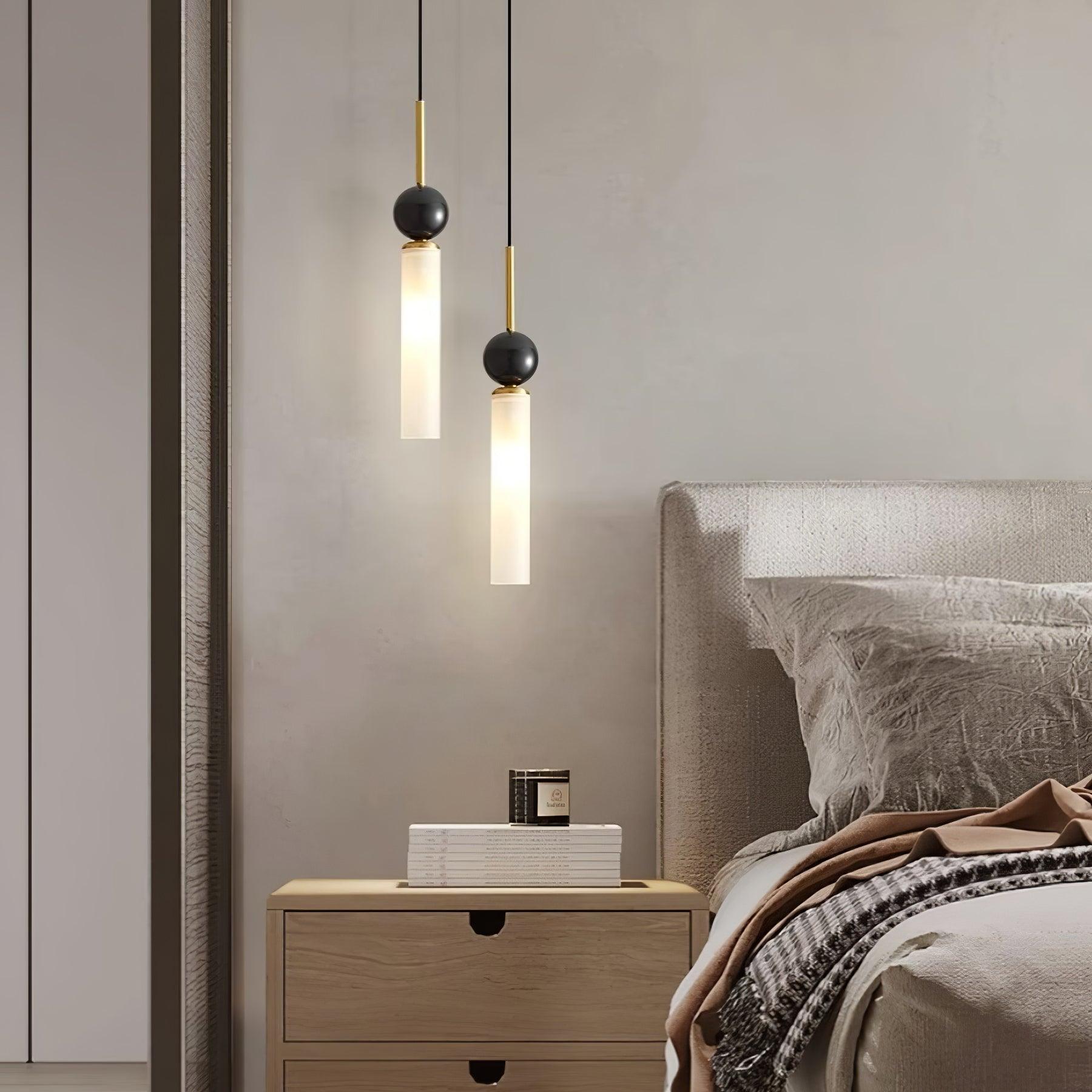 Two brass-stem dark-sphere pendants beside upholstered bedhead and wood nightstand with books and candle