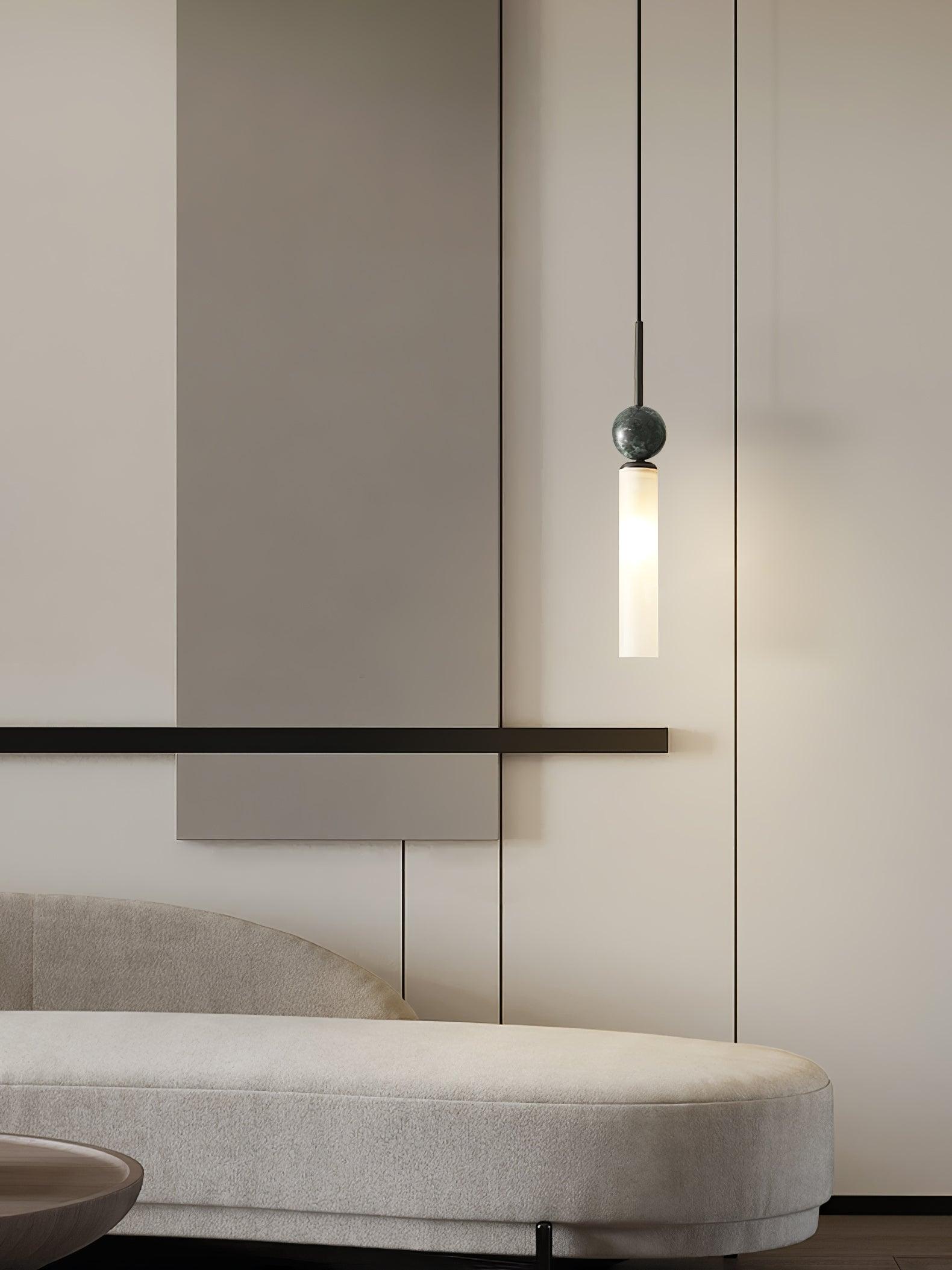 Black marble-sphere pendant with lit white tube above rounded pale sofa, with partial round wood table below