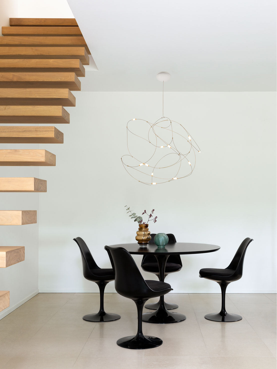 Rounded wire-loop pendant above a black dining table beside an open wooden staircase