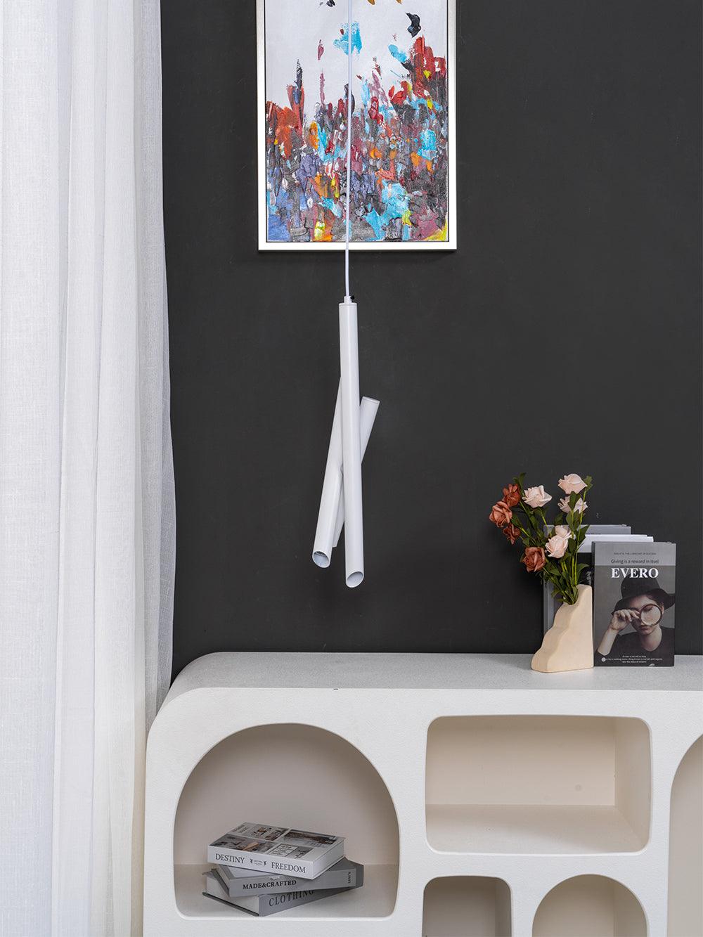 Closer view of a white Tubes pendant above a curved cabinet with flowers and a small framed picture
