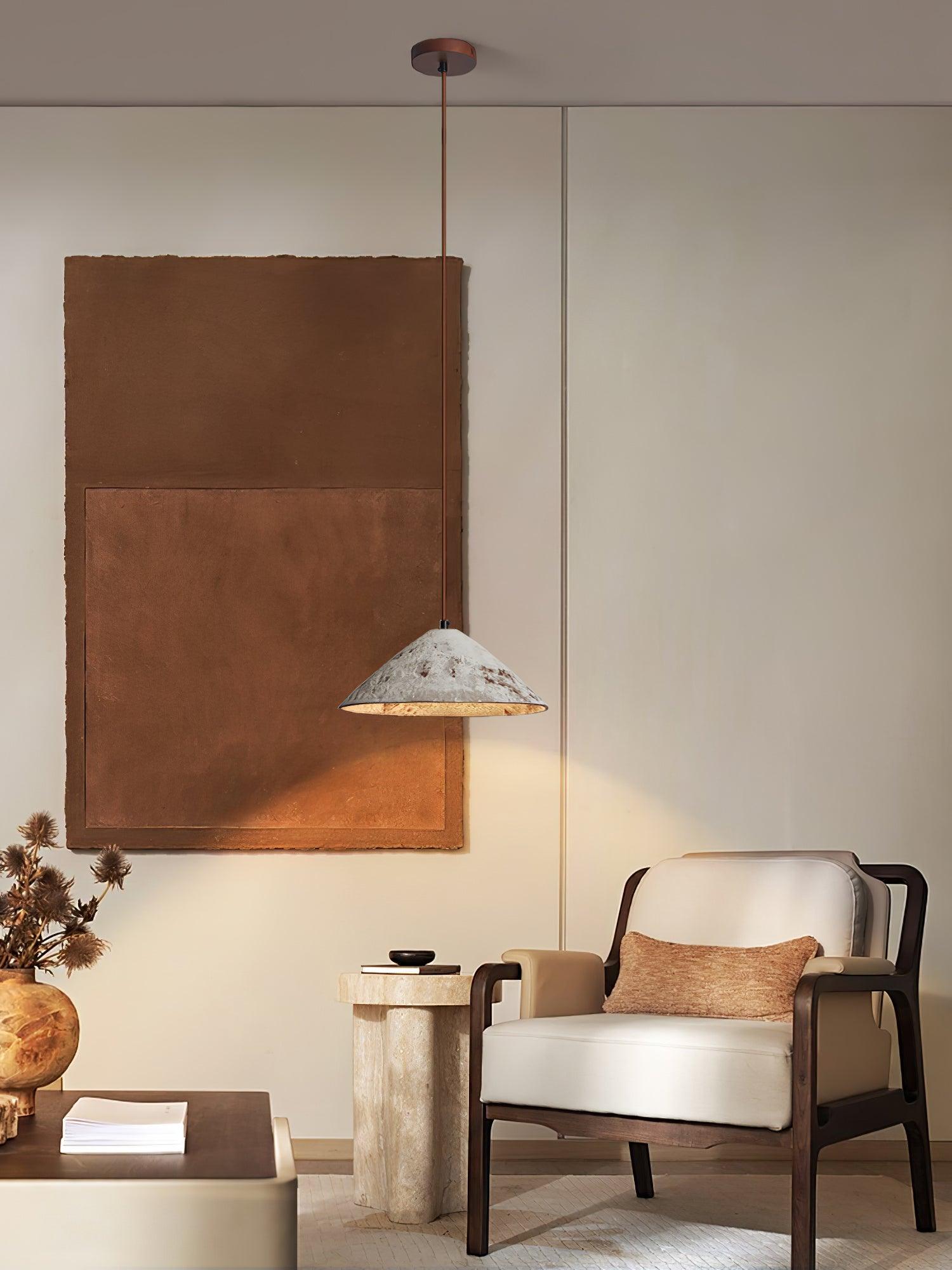 White ceramic pendant beside a cream armchair, with a brown ceiling canopy, large brown artwork and stone pedestal