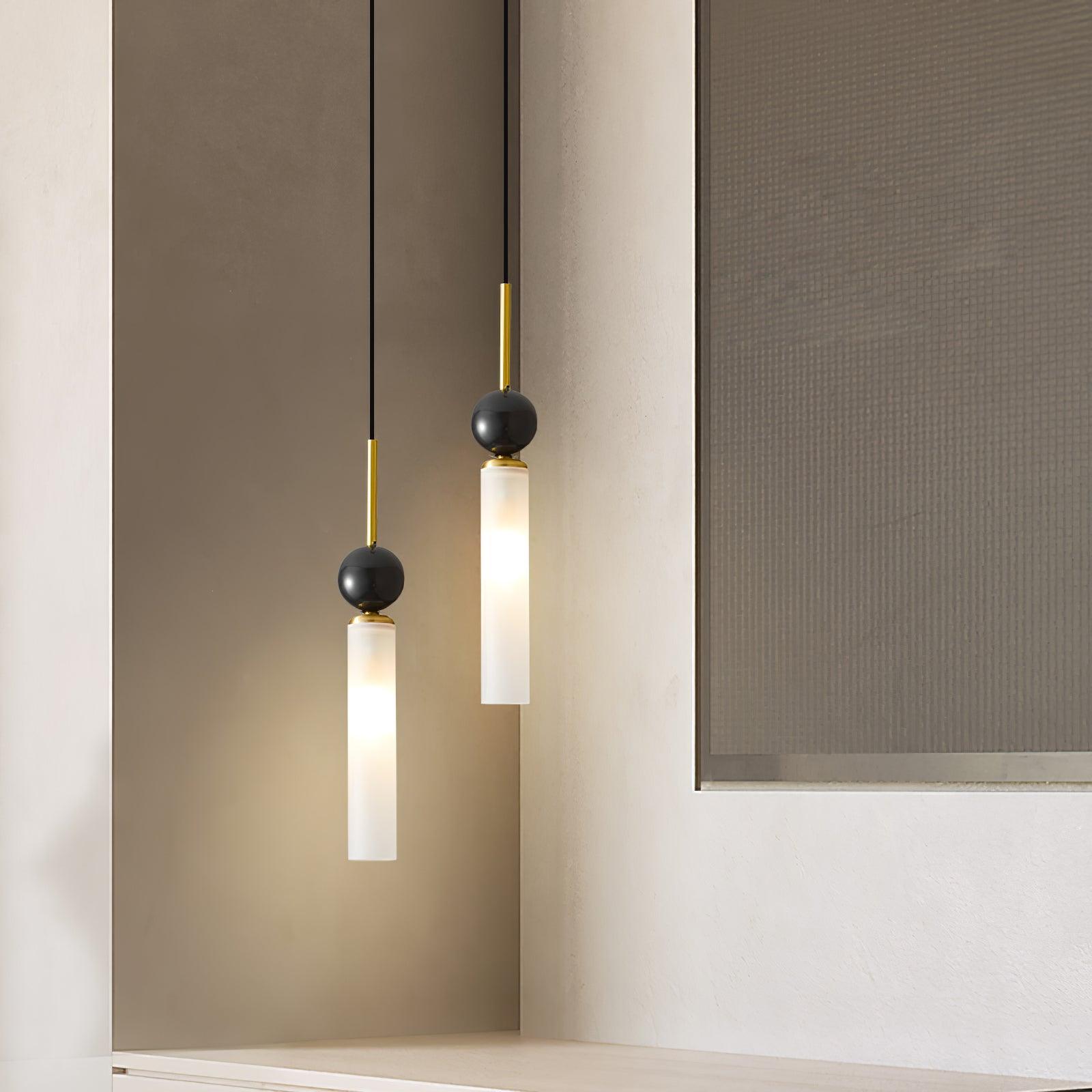 Close view of two staggered brass-stem dark-sphere pendants and glowing white tubes beside textured framed artwork