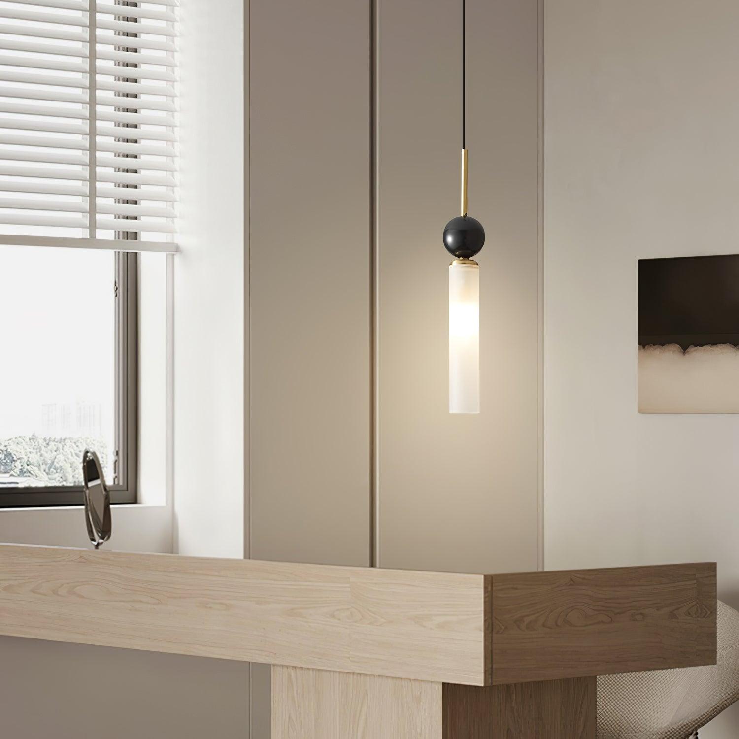Closer desk-room view of brass-stem dark-sphere pendant, white tube, wood desk and small mirror beside window blinds