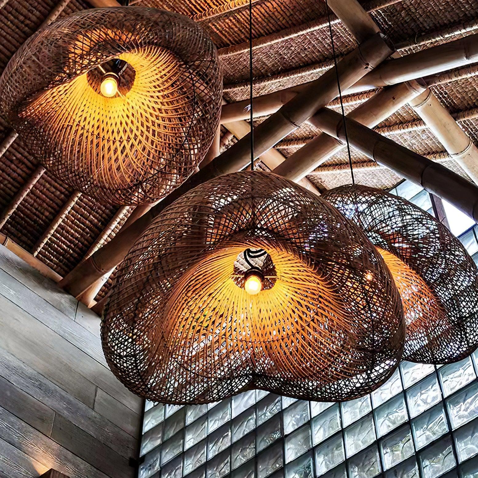 Upward view of three glowing bulbs inside wave-shaped woven shades beneath a woven roof beside glass blocks