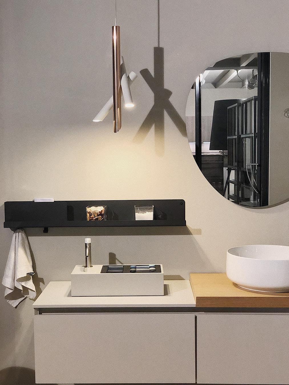 White and rose-gold Tubes pendant beside a round mirror above a washbasin