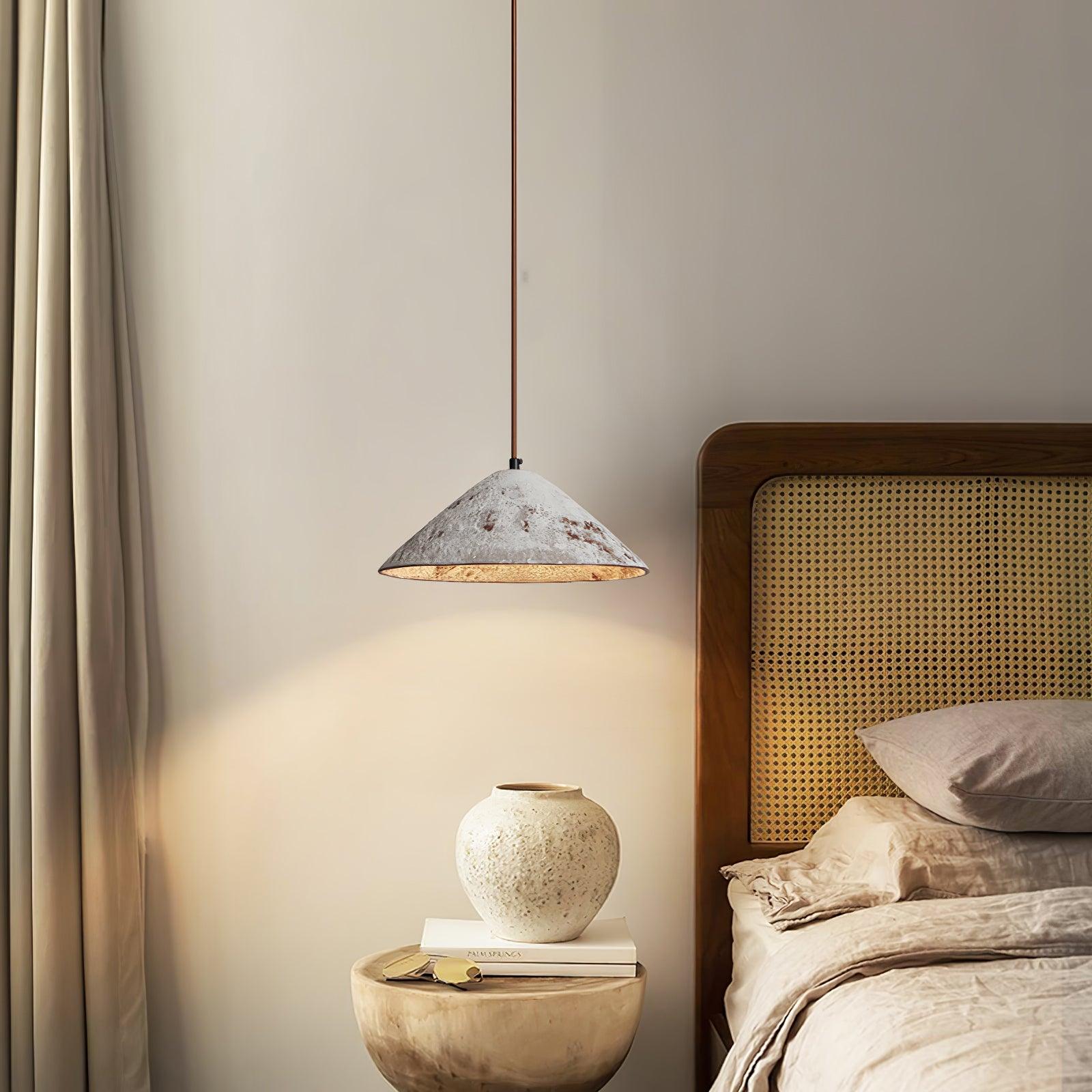 White textured cone pendant beside a woven wood headboard, above a round stone table with a white vase and book