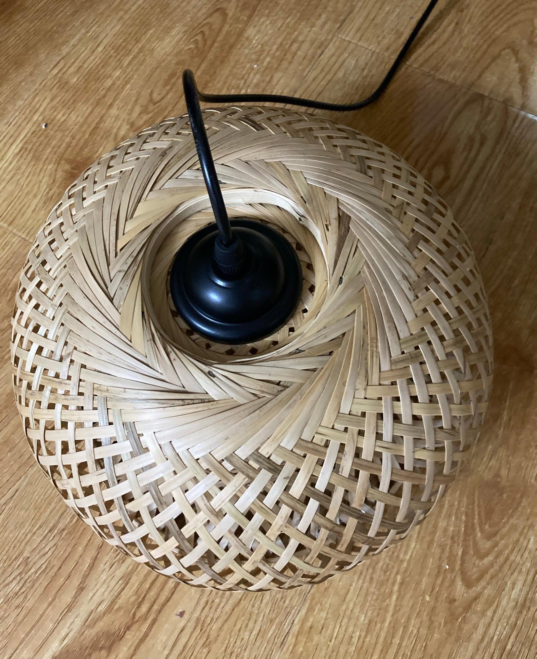 Top view of unlit bamboo shade on wooden floor, with interlaced strips around black central fitting and cable