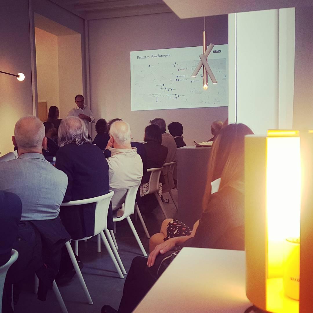 White and rose-gold Tubes pendant in a room with seated attendees and a projected presentation
