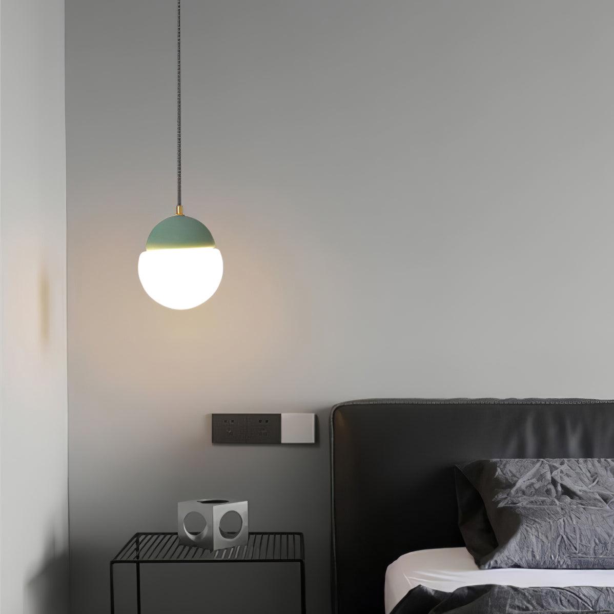 Green-capped pendant beside a dark bed