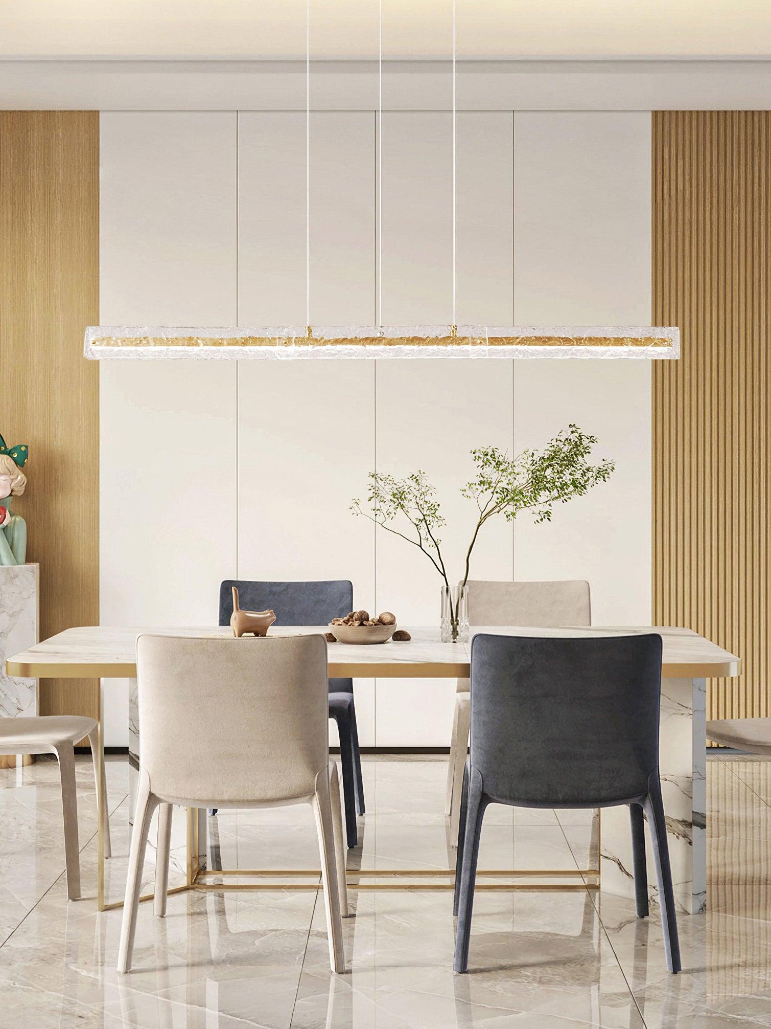 Clear rectangular textured-glass pendant above a pale dining table, mixed chairs and a leafy vase