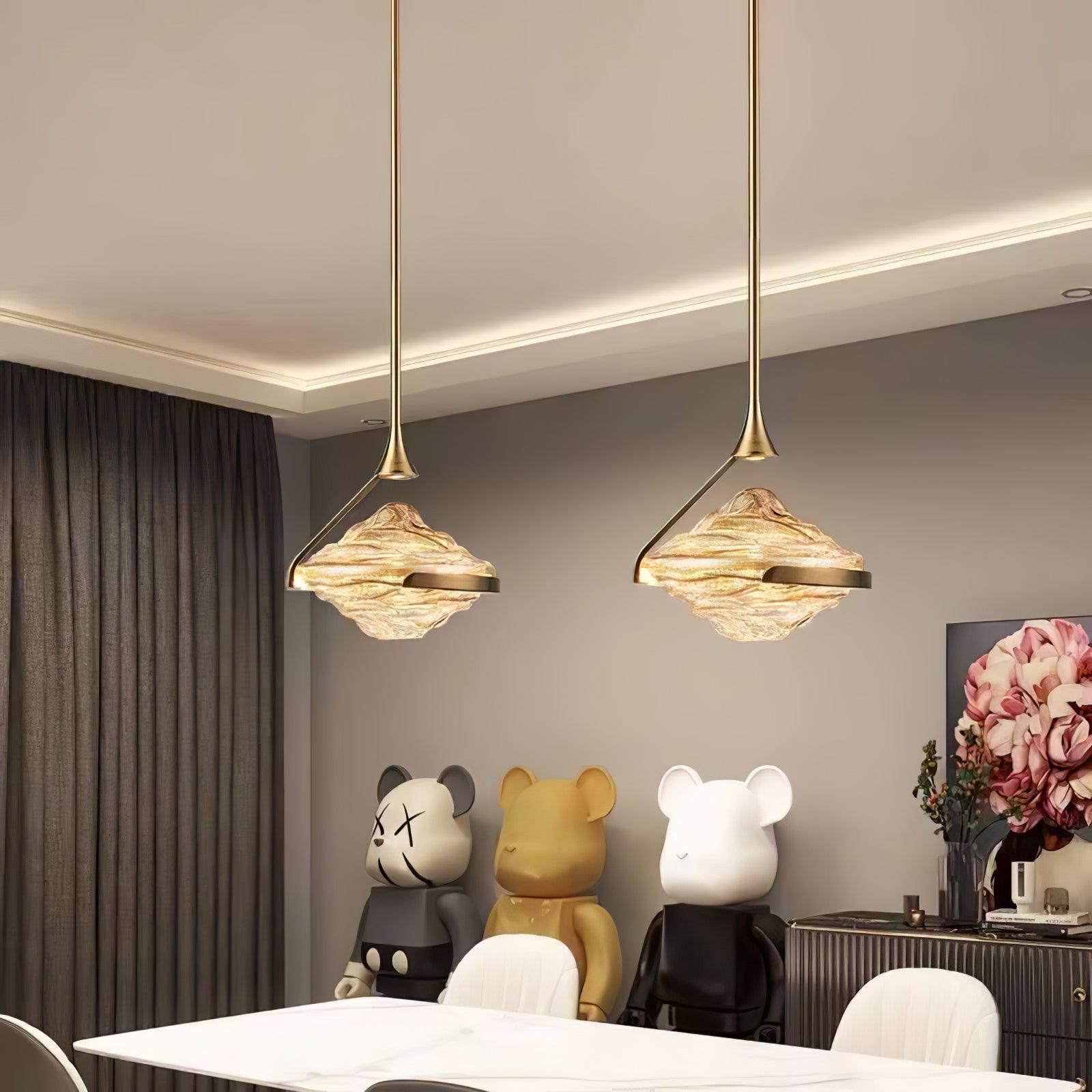 Two gold-toned glass pendants above a pale dining table with white chairs, bear-shaped figures and flower artwork