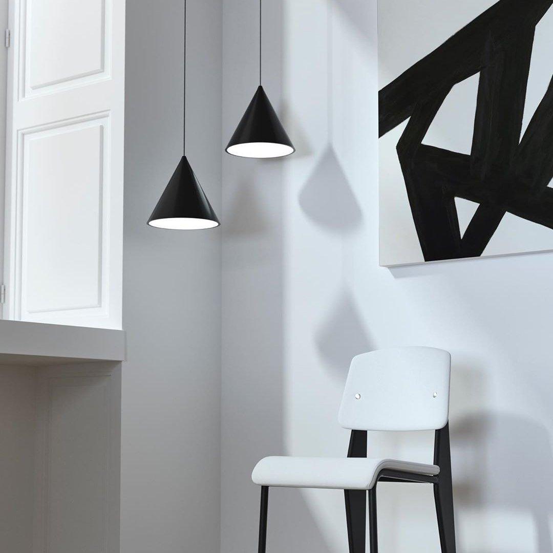 Two black conical pendants at different drops beside a white chair, black wall artwork and bright window