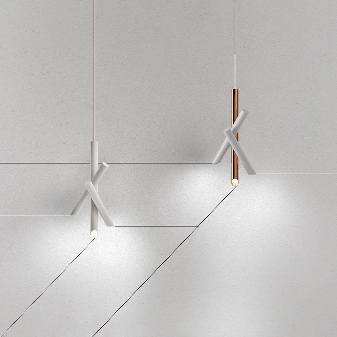 White and rose-gold Tubes pendants at different hanging levels against pale geometric wall panels
