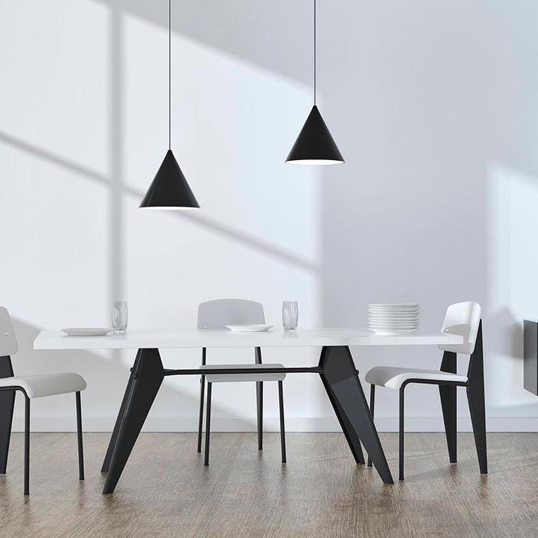 Two black conical pendants over a white dining table with wood edge, white chairs, glasses and stacked dishes