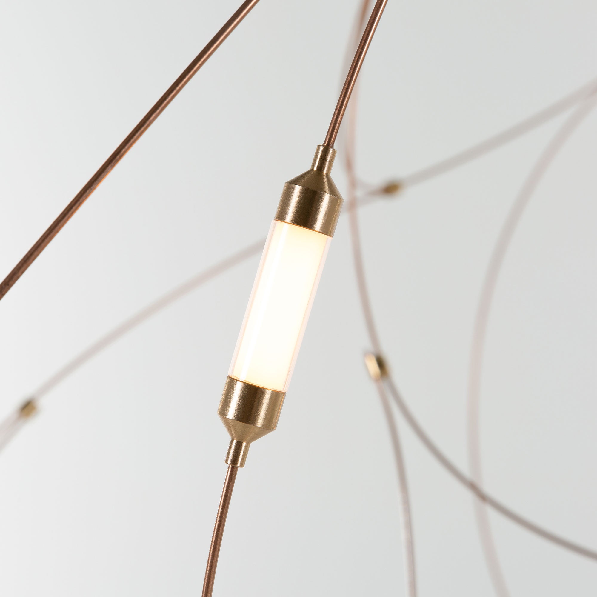 Gold-tone capped cylindrical diffuser on a thin brown-tone wire against a pale background