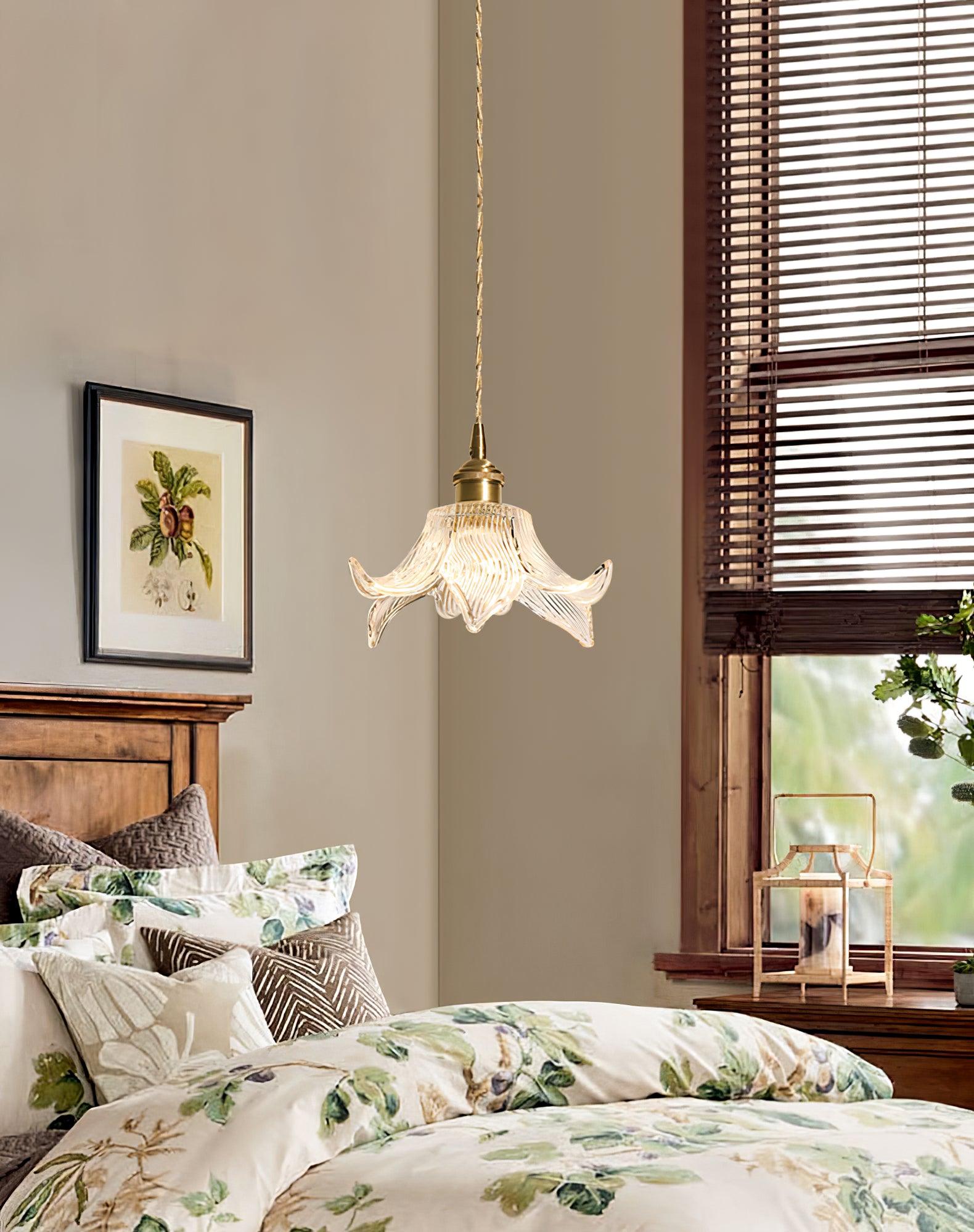 Lit flower glass pendant beside a timber headboard, green floral bedding and a wooden window with dark blinds.
