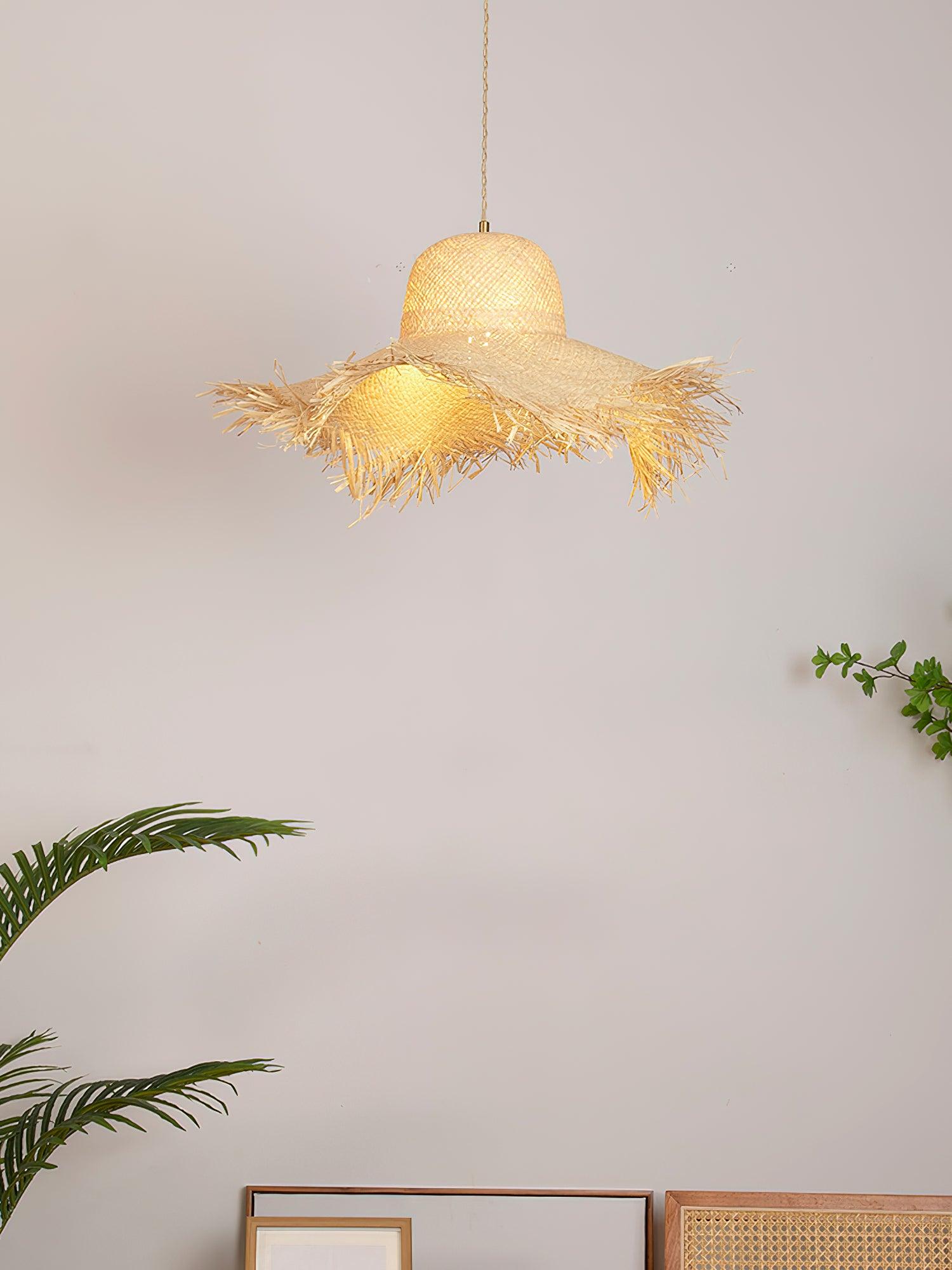 Pale-lit rattan hat shade above leaning picture frames and cane furniture, with green plants on both sides