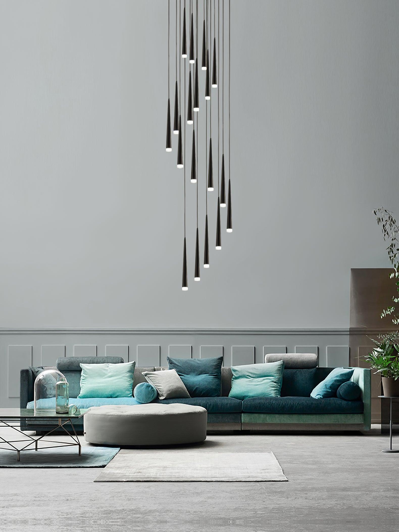 Long cascade of illuminated black tapered tubes above a teal sofa in a tall living room