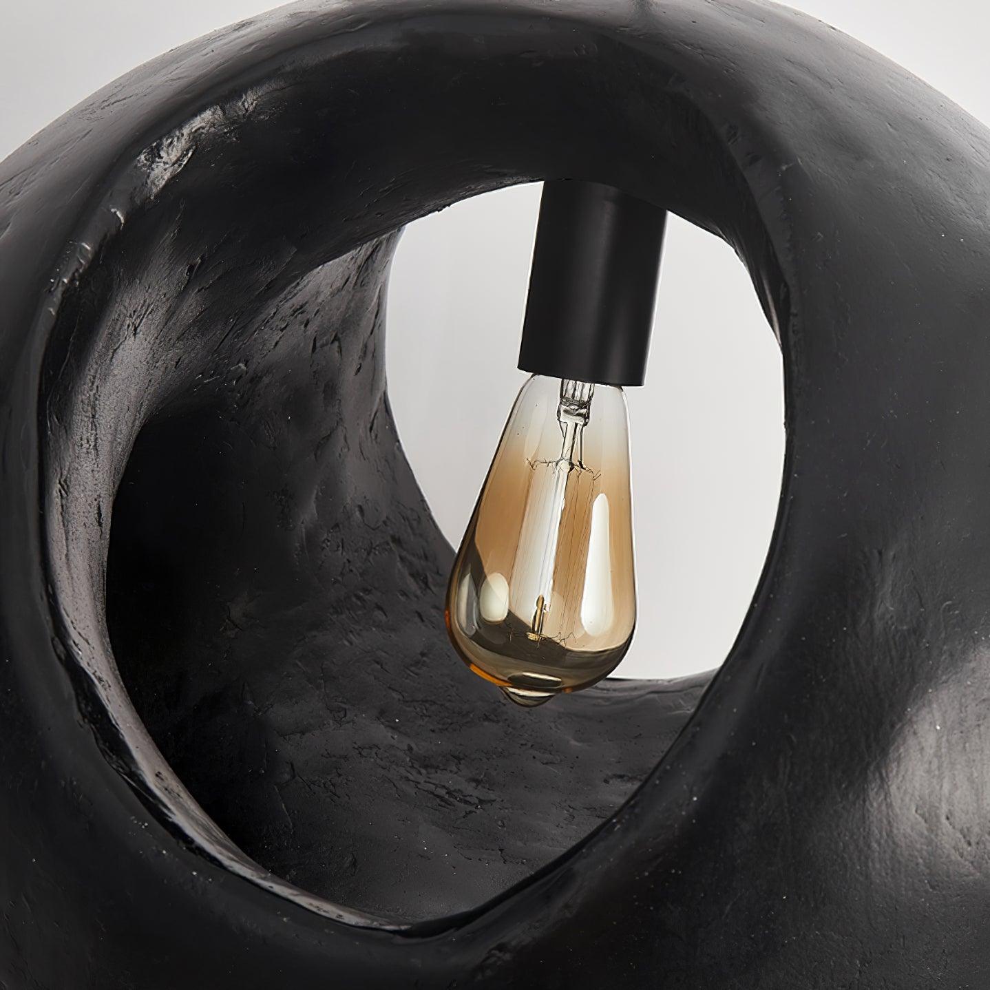 Close-up through an oval shade opening showing a teardrop filament bulb in a black holder and dark textured inner rim