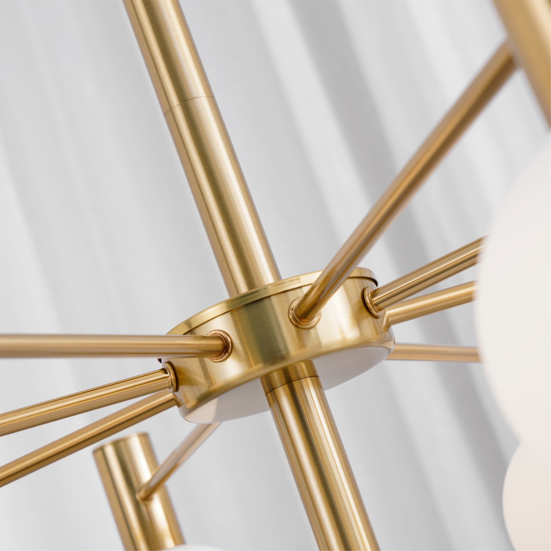 Close view of the gold-tone circular chandelier hub, radial arms and vertical rod with a visible joint.