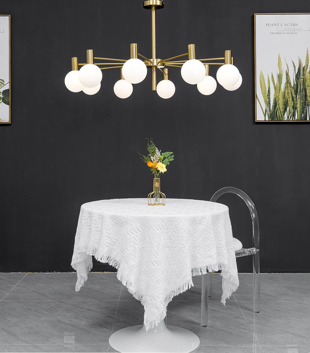 Front view of a lit white-globe chandelier above a white-cloth dining table and clear chair, with botanical prints behind.