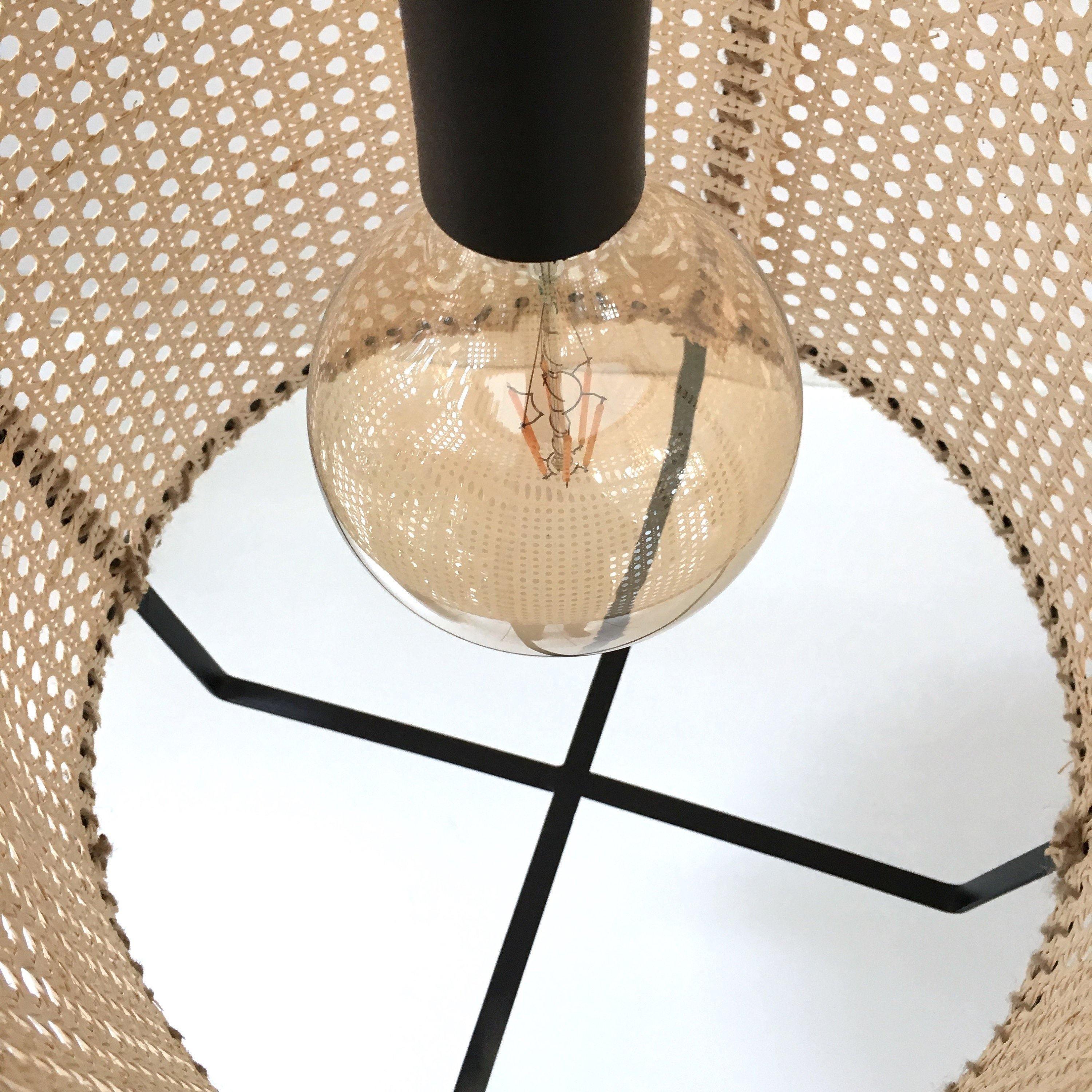Upward close-up through the cane shade showing a clear globe bulb and crossed black lower frame
